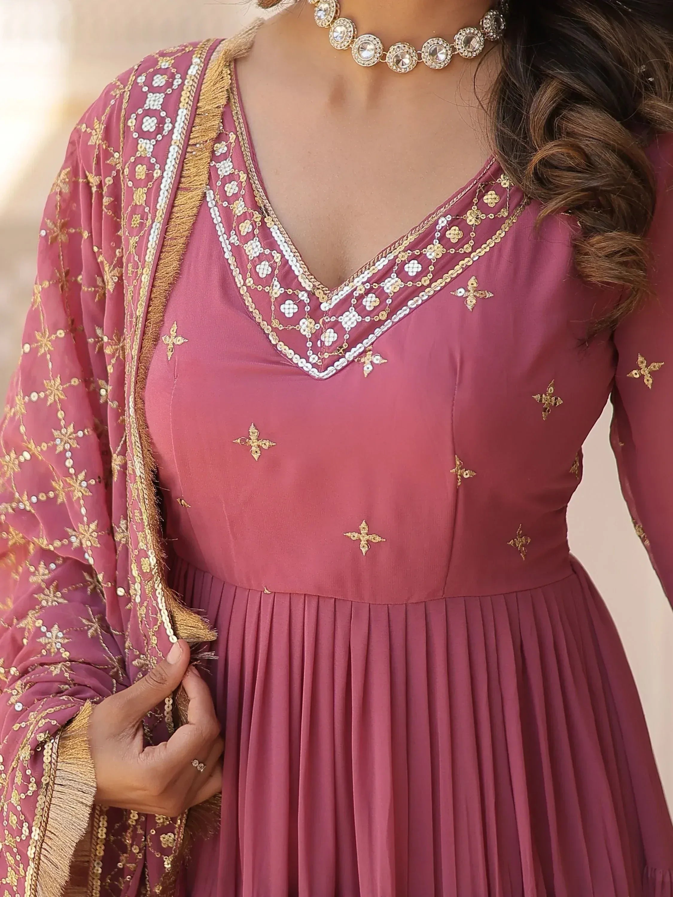 Pink ethnic gown with gold embroidery, V-neck, and pleated skirt, paired with matching dupatta and statement necklace