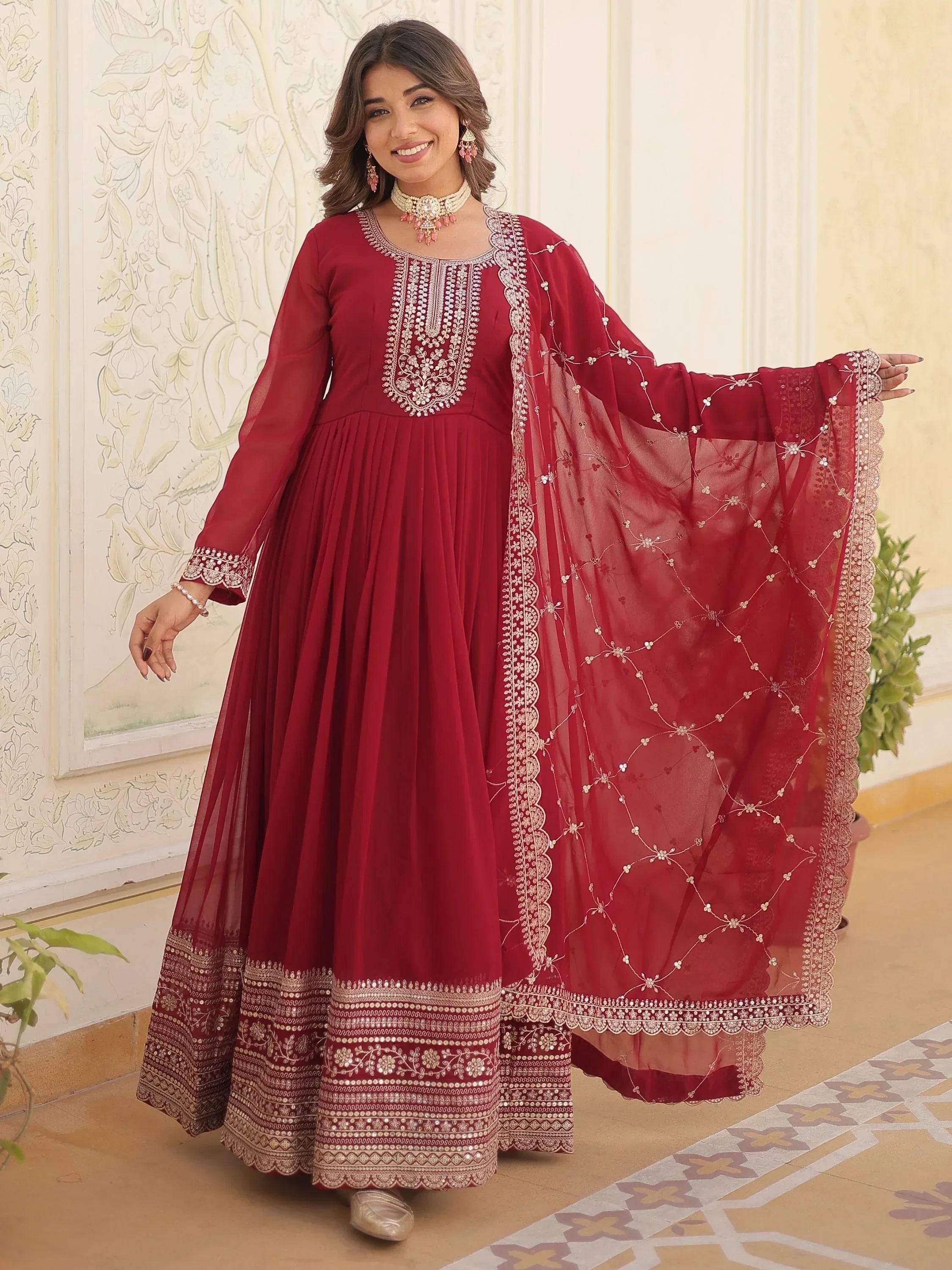 Woman wearing maroon embroidered Anarkali suit with net dupatta and ethnic jewelry