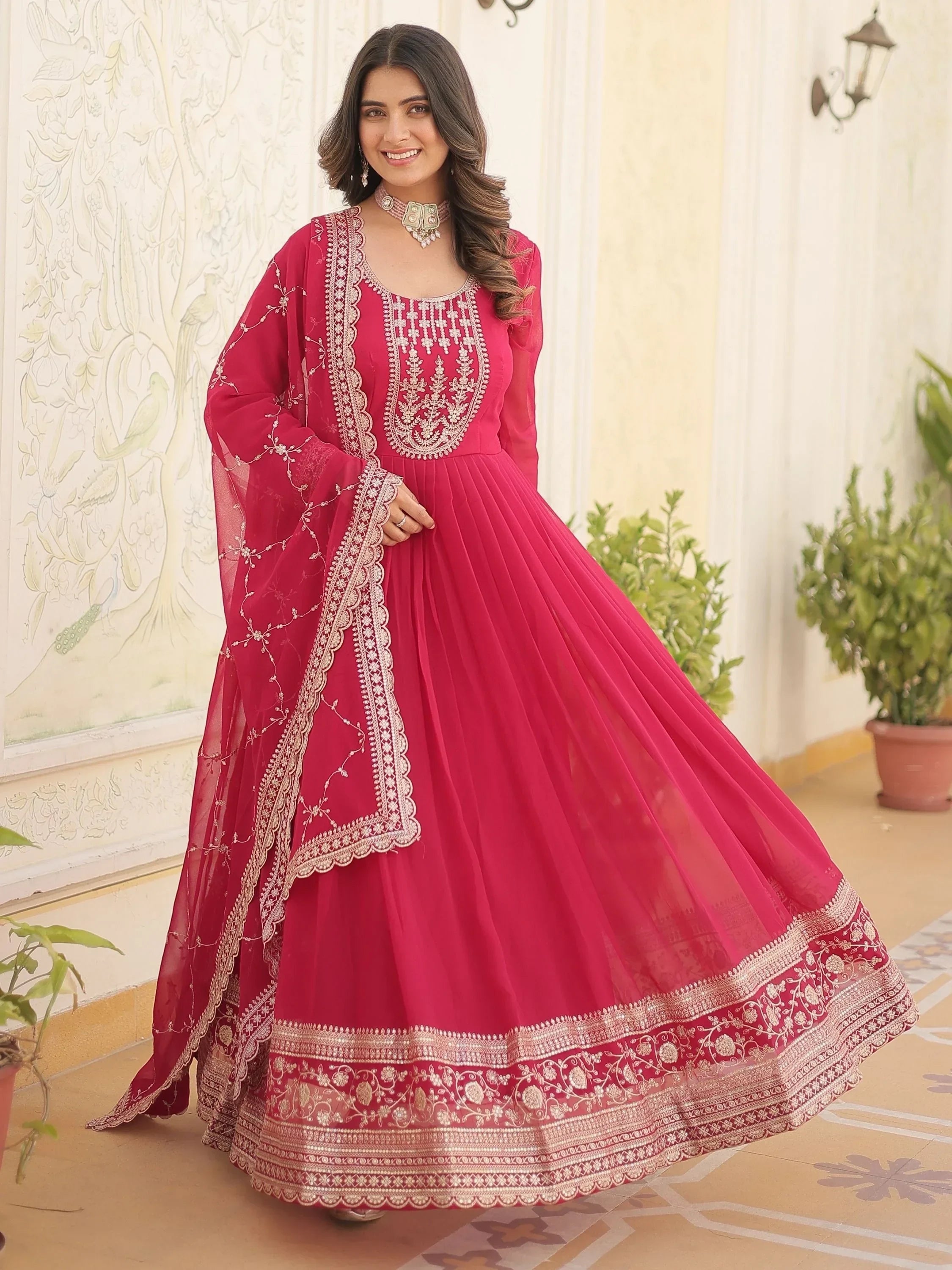 Woman wearing a pink embroidered ethnic gown with dupatta, standing in a courtyard