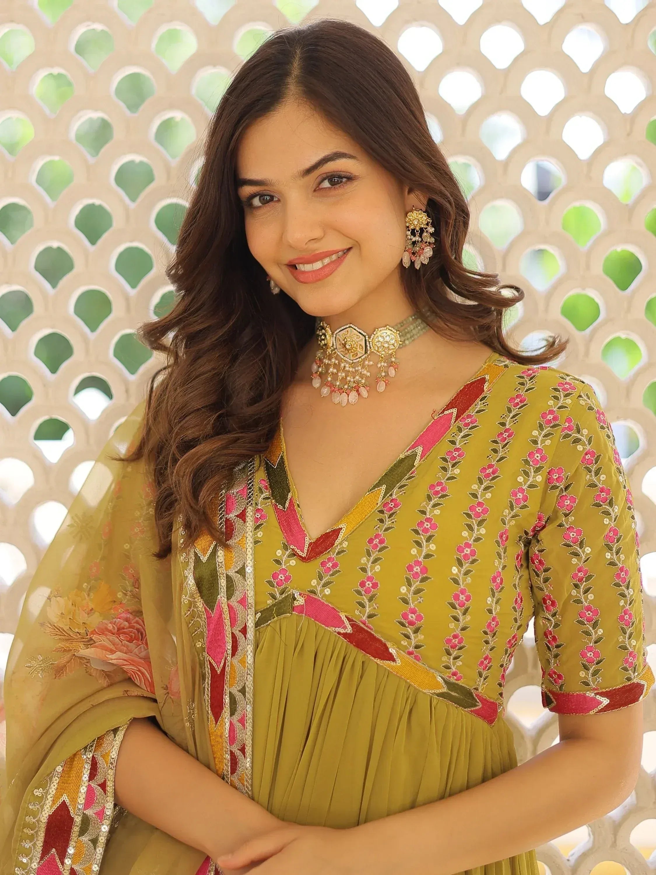 Woman in olive green floral embroidered ethnic gown with pink and gold detailing, paired with traditional jewelry.