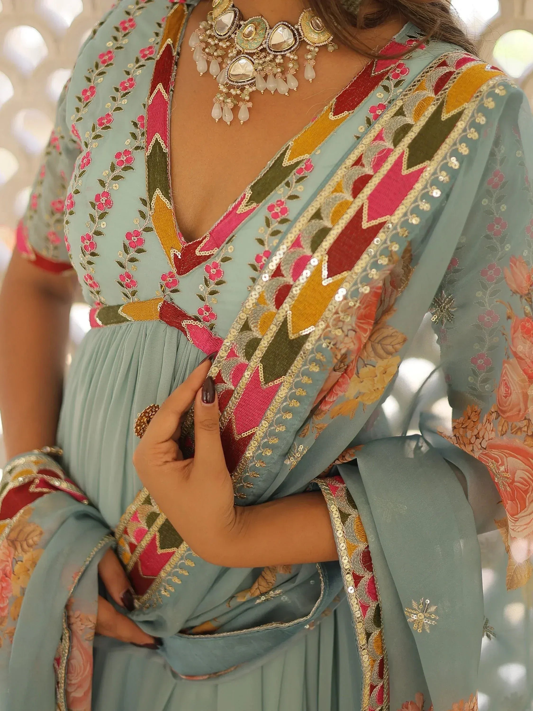 Mint green ethnic gown with floral embroidery, mirror work, and colorful patchwork detailing, paired with statement jewelry.