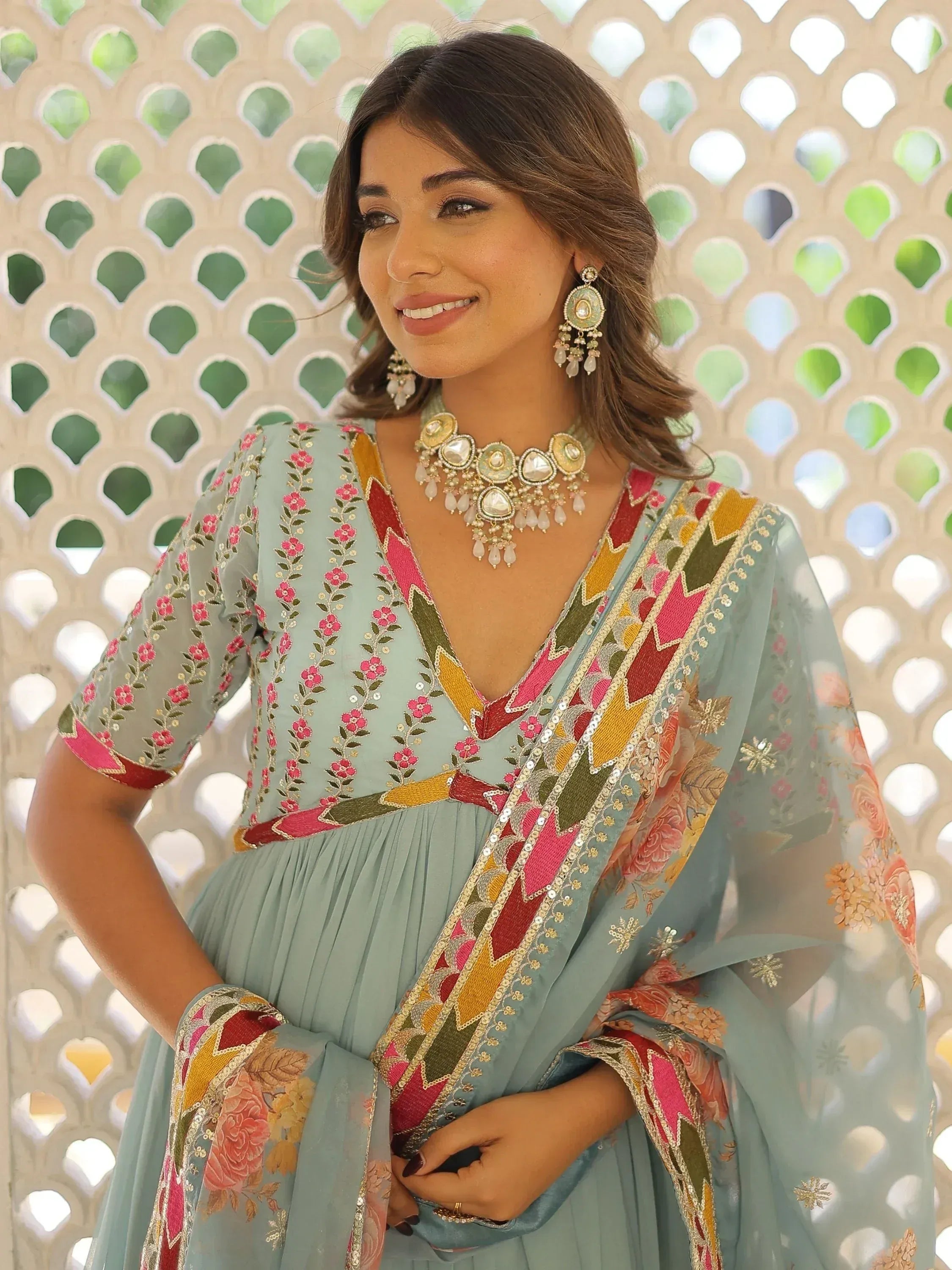 Woman in embroidered mint green salwar kameez with floral and geometric detailing, paired with statement jewelry
