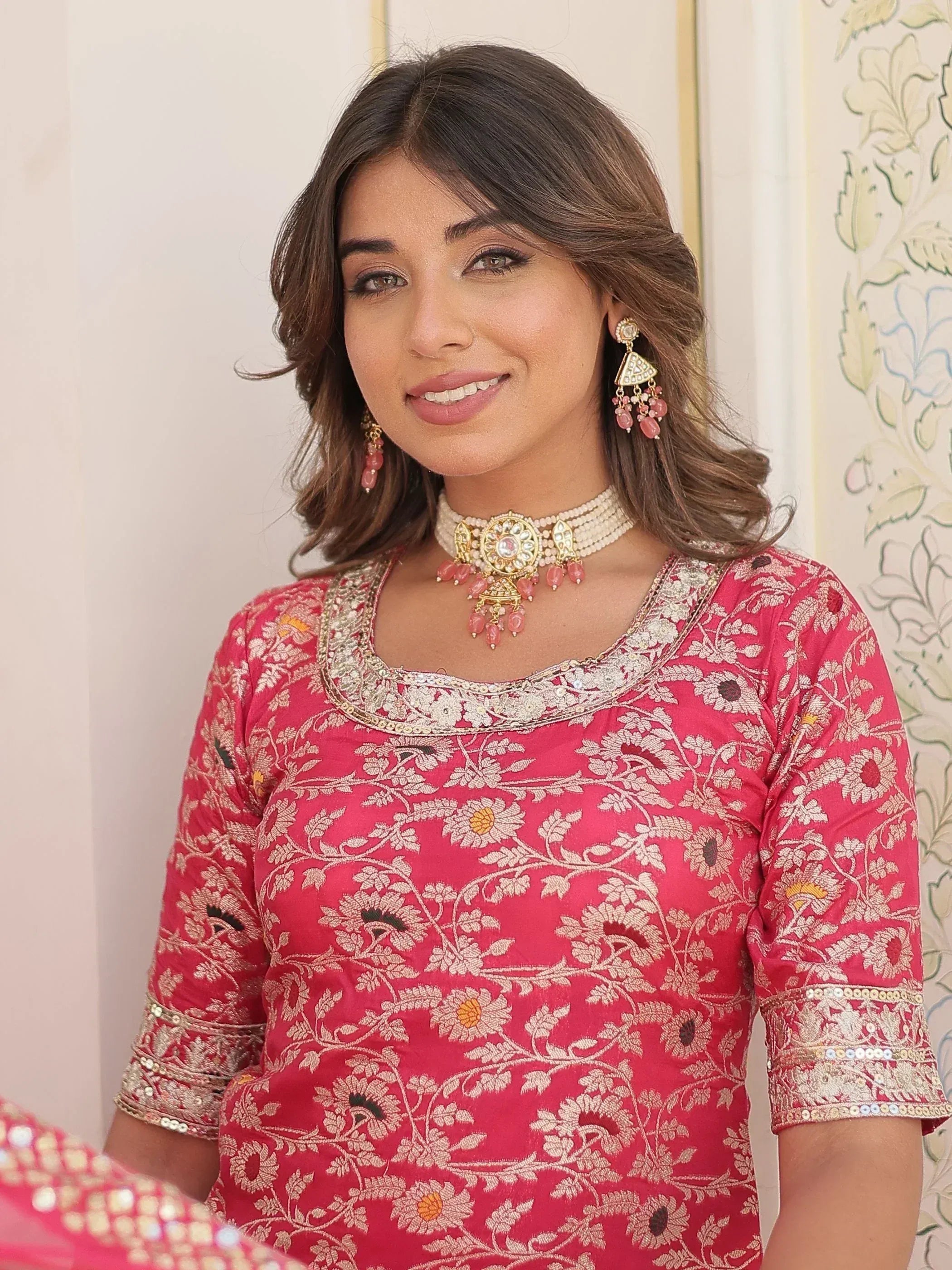 Woman in pink floral embroidered Indian ethnic top with gold jewelry, perfect for festive occasions.