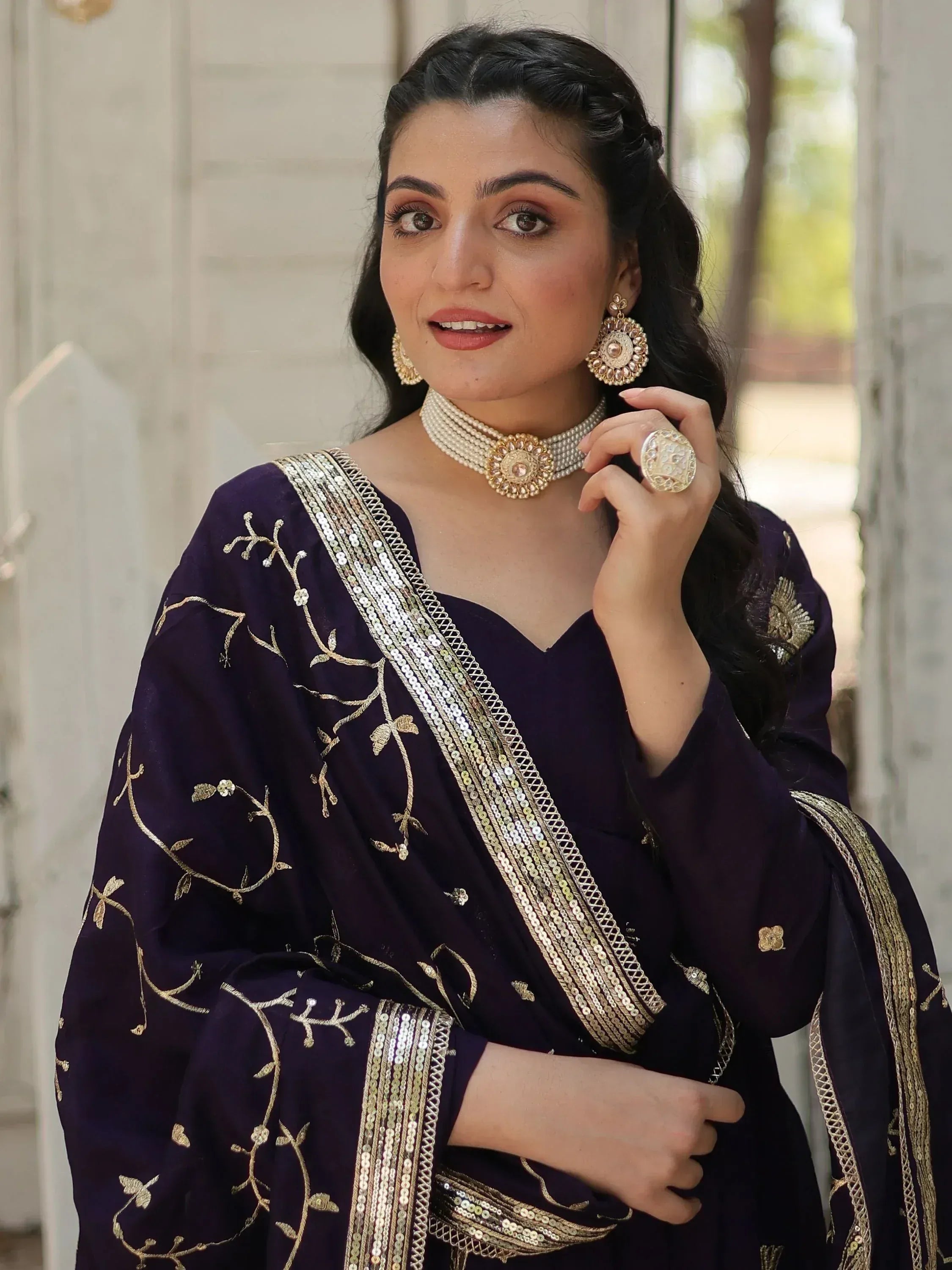 Elegant purple ethnic gown with gold embroidery and sequin detailing, paired with traditional jewelry.