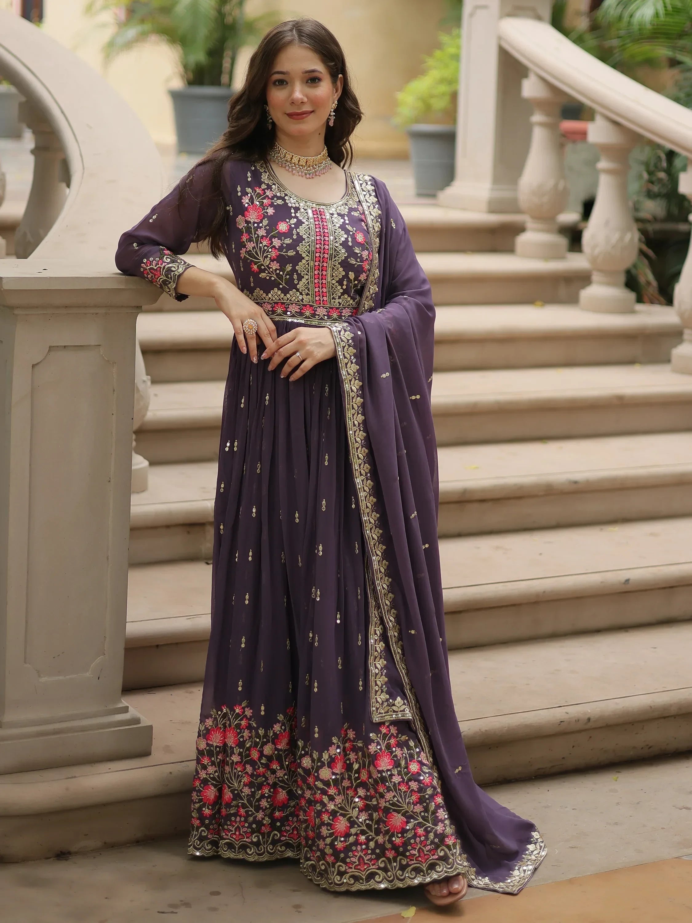 Woman in purple embroidered ethnic gown with floral patterns and dupatta on staircase