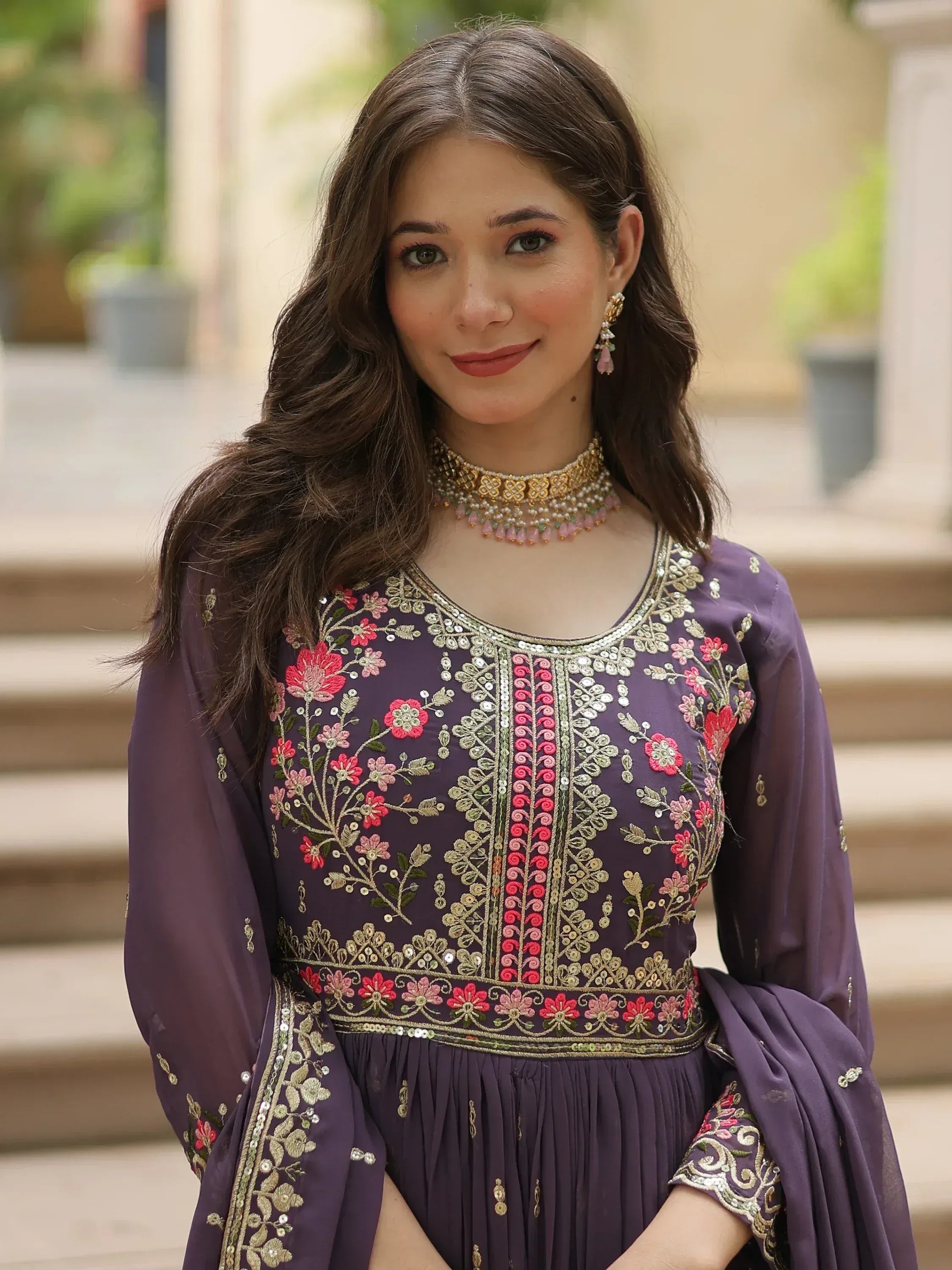 Woman wearing purple embroidered ethnic gown with floral patterns and gold jewelry