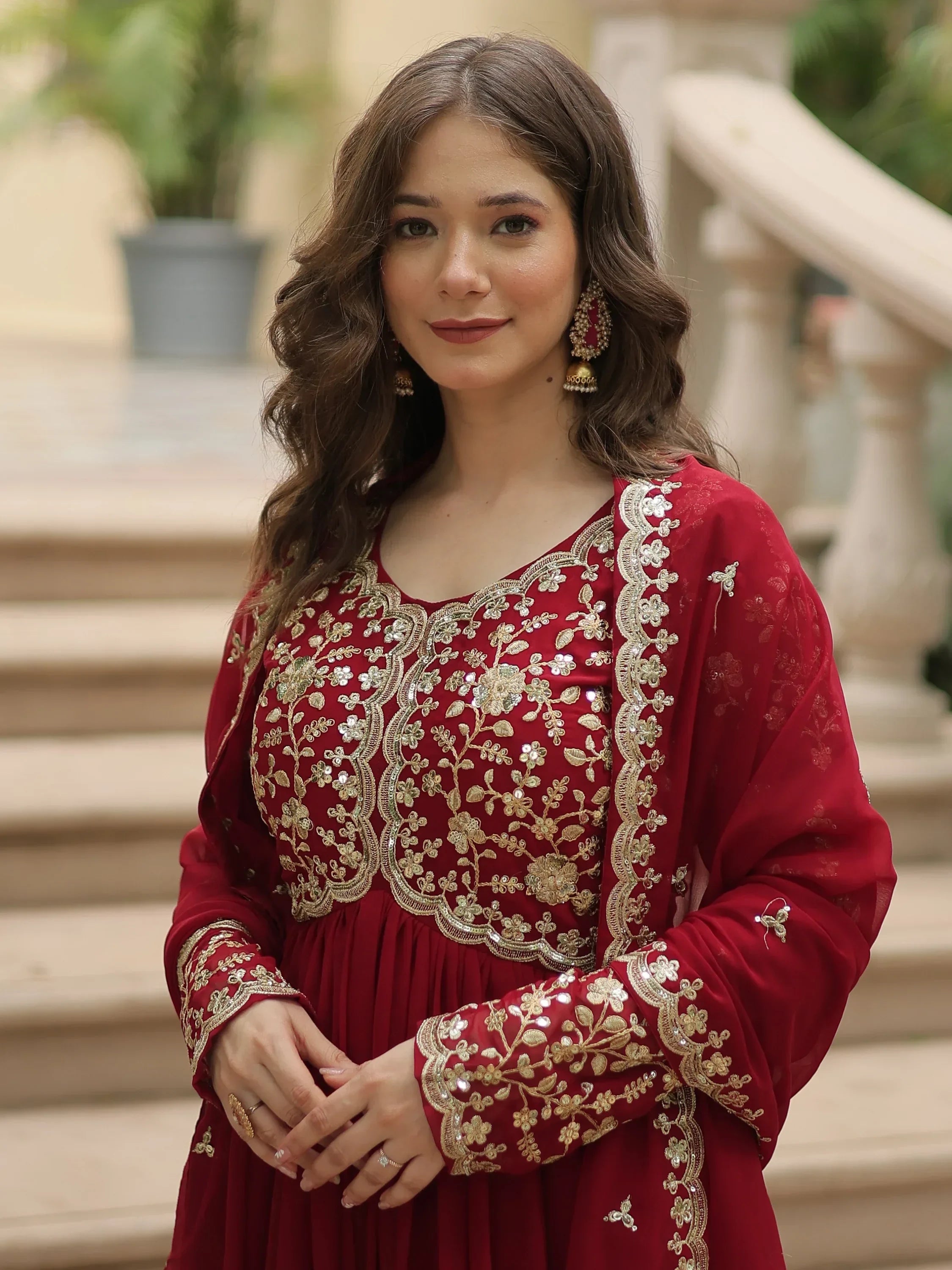 Woman wearing a red embroidered Indian ethnic gown with gold floral detailing outdoors