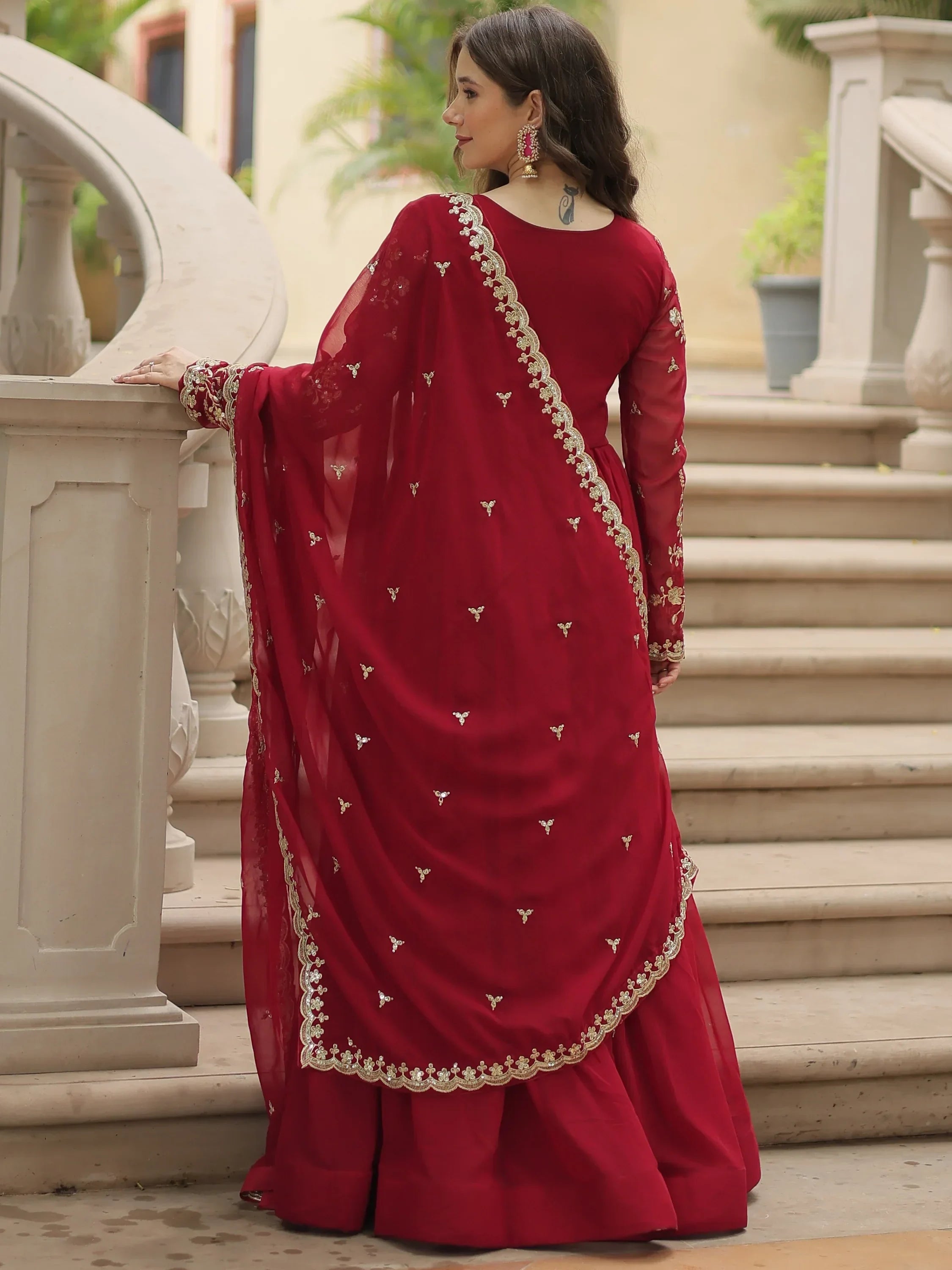 Woman in red embroidered lehenga choli and dupatta posing on stone staircase