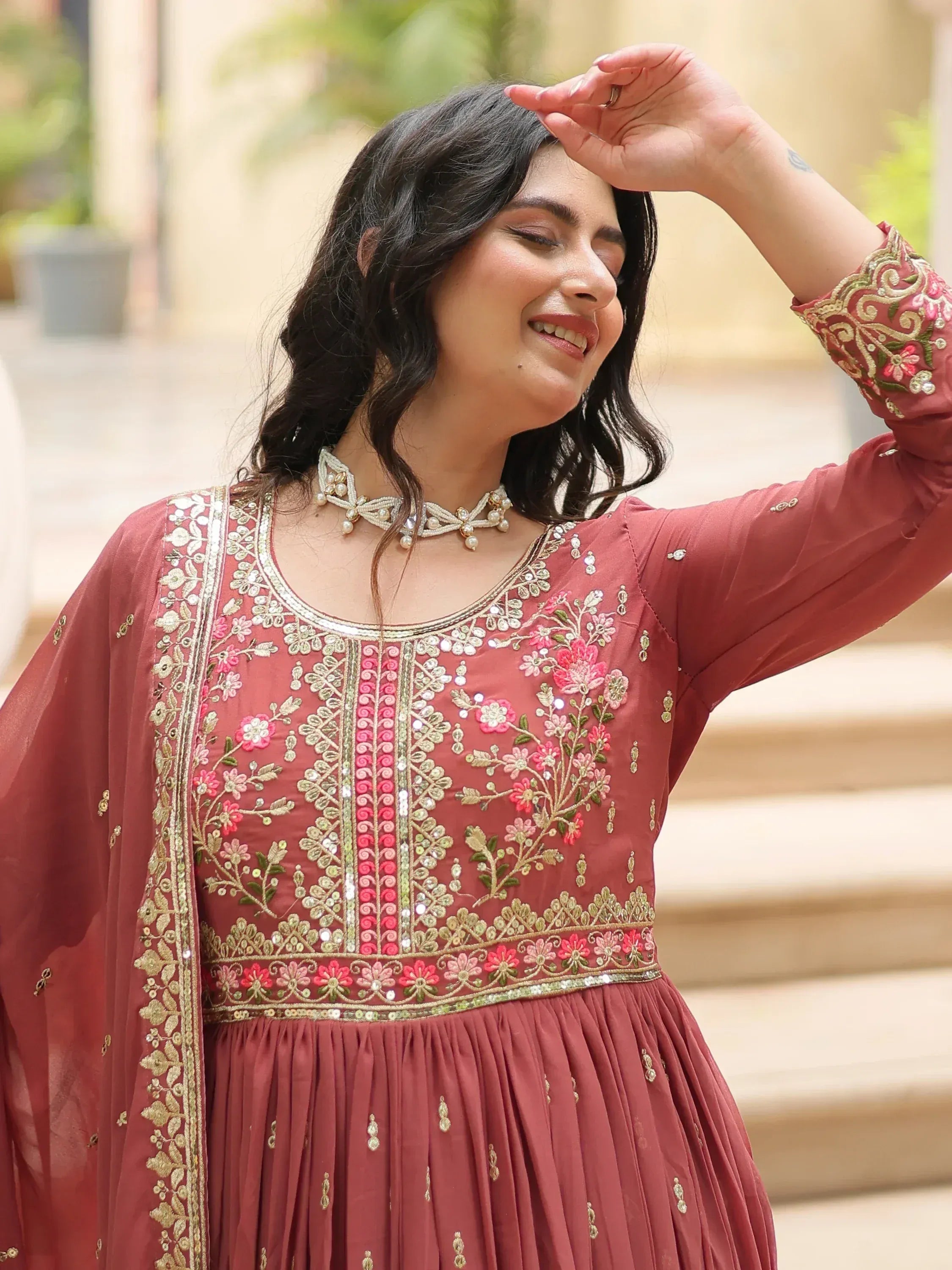 Woman in maroon embroidered ethnic gown with floral detailing and matching dupatta, perfect for Indian occasions.