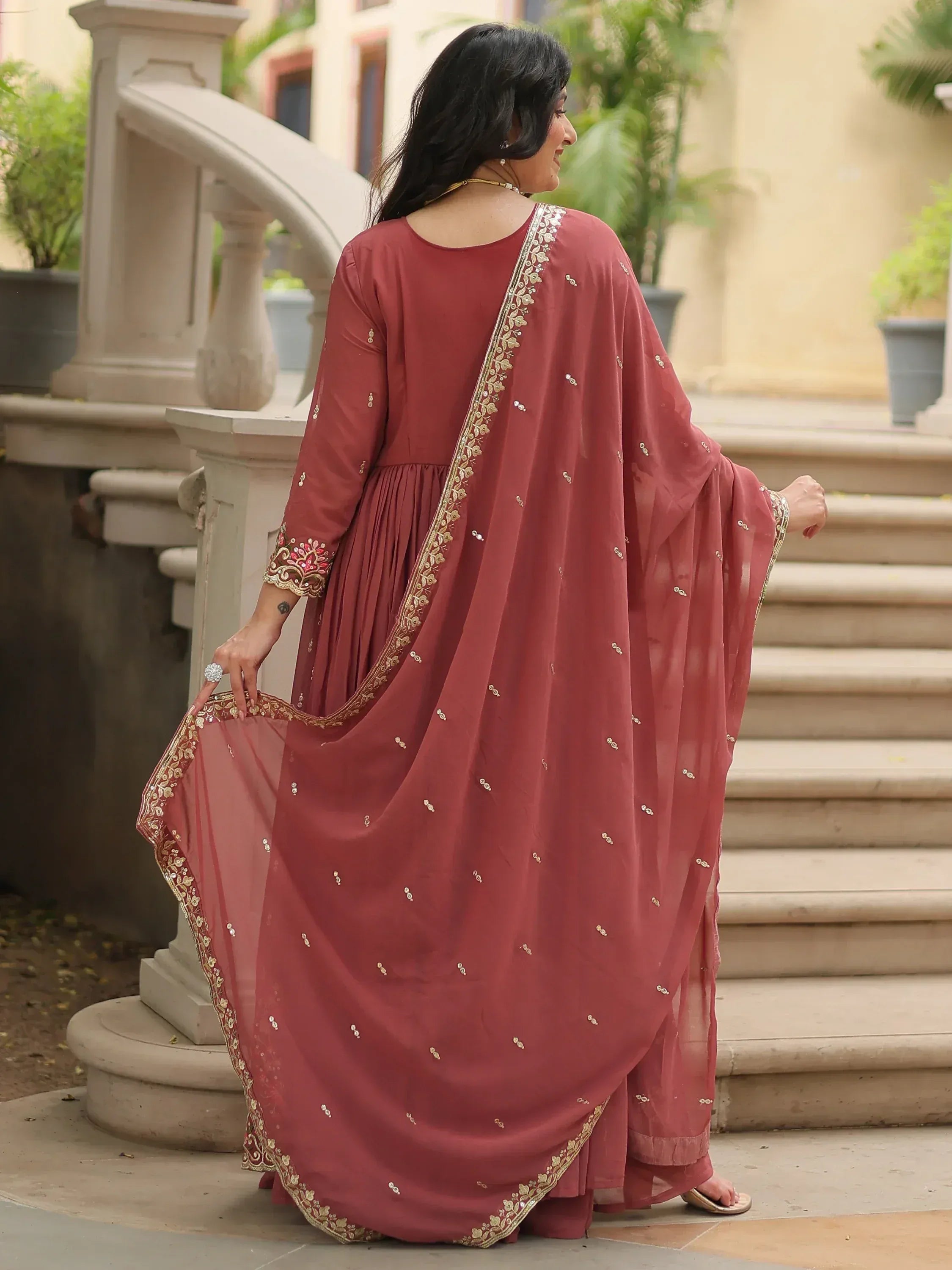 Woman in maroon ethnic gown with gold embroidery, perfect for Indian occasions and festive wear.