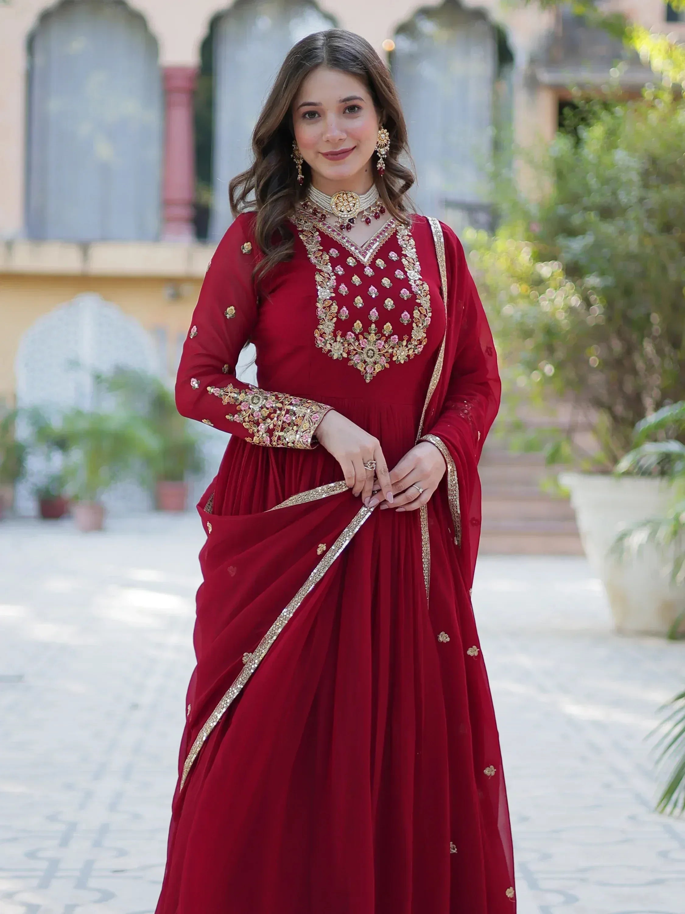 Woman in maroon embroidered Indian ethnic gown with gold detailing, perfect for weddings and festive occasions.