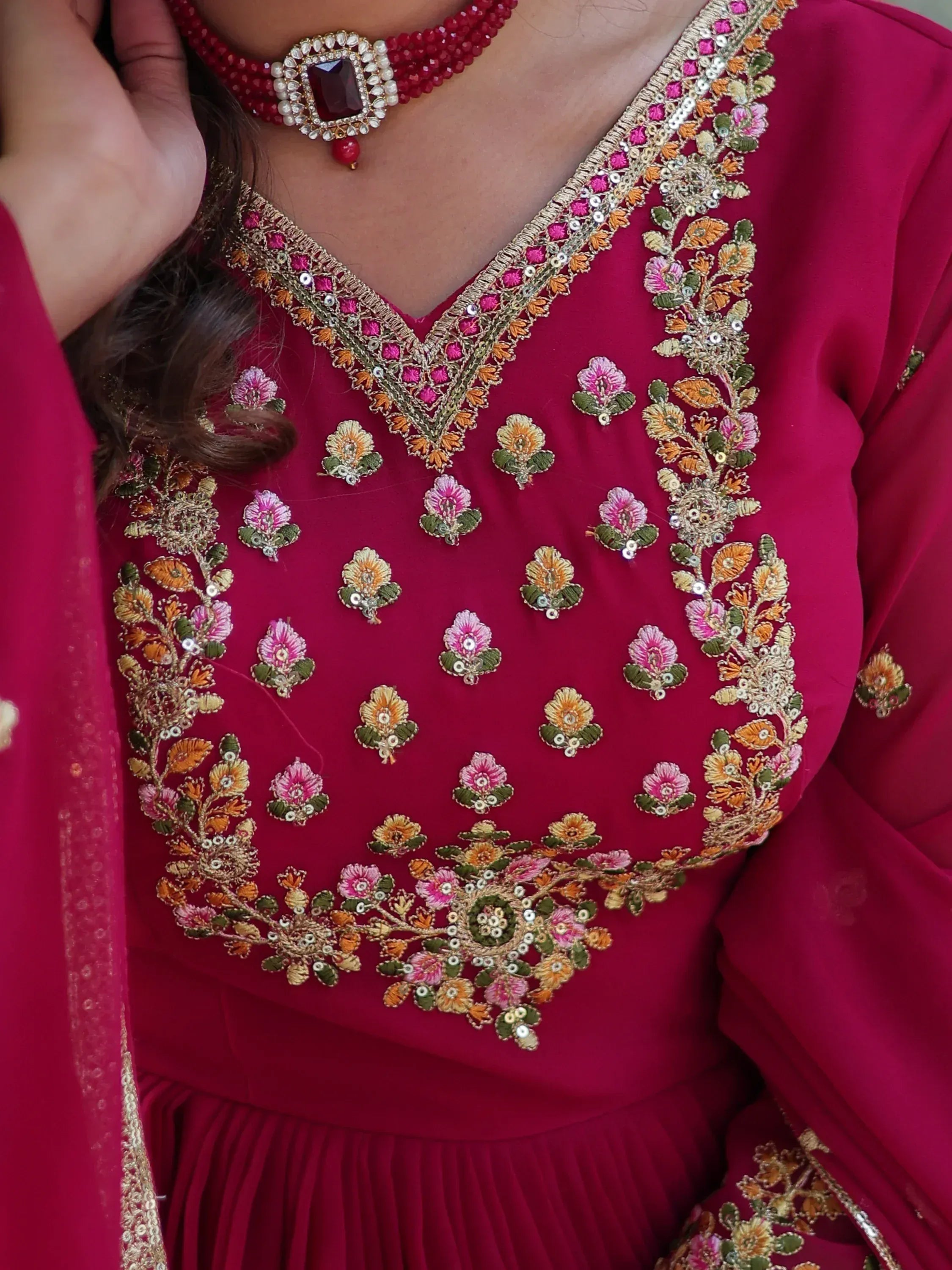 Richly embroidered maroon ethnic gown with floral motifs and matching jewelry, perfect for Indian celebrations.