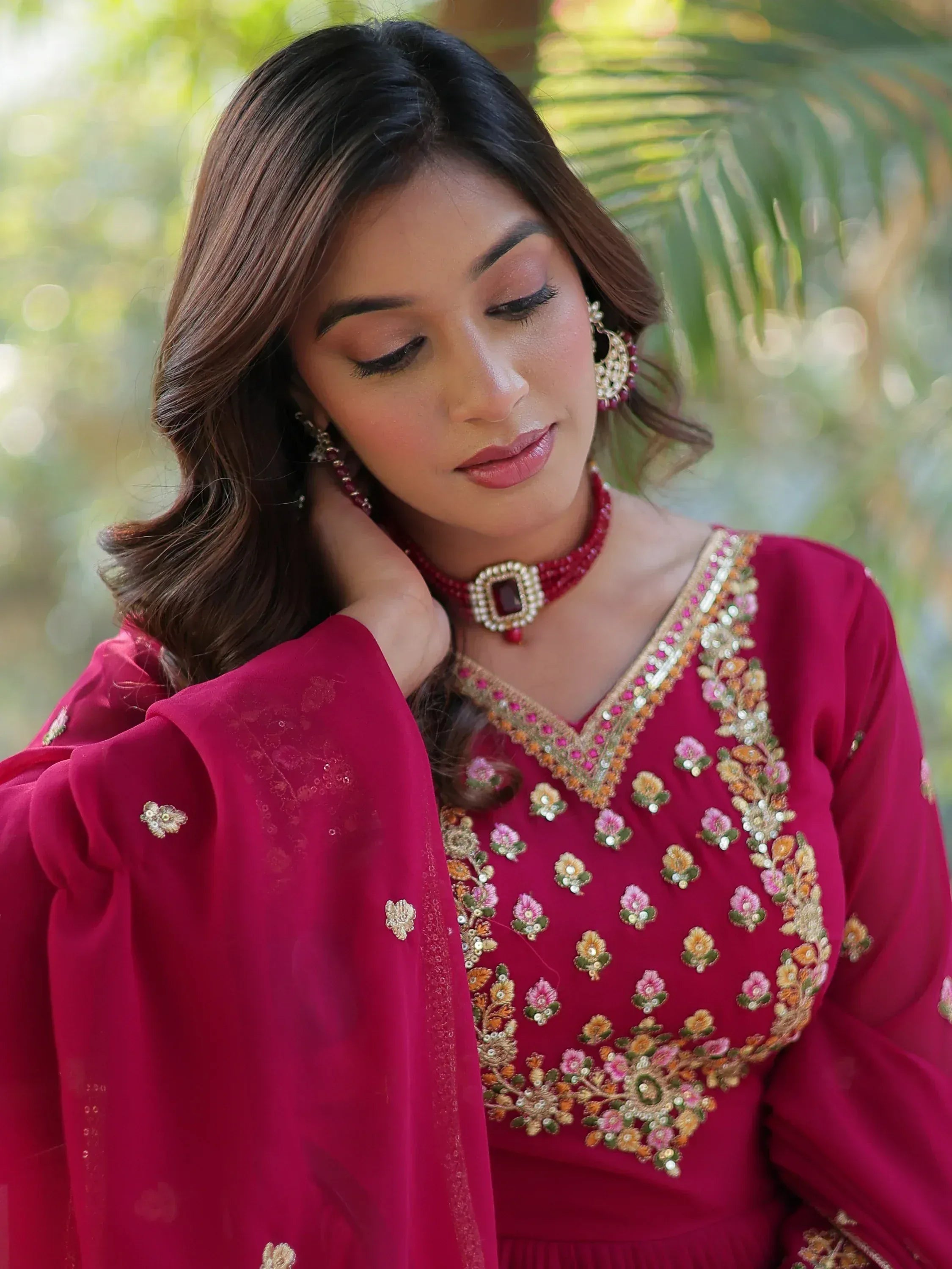 Woman in maroon embroidered ethnic gown with floral detailing and matching jewelry, perfect for Indian occasions