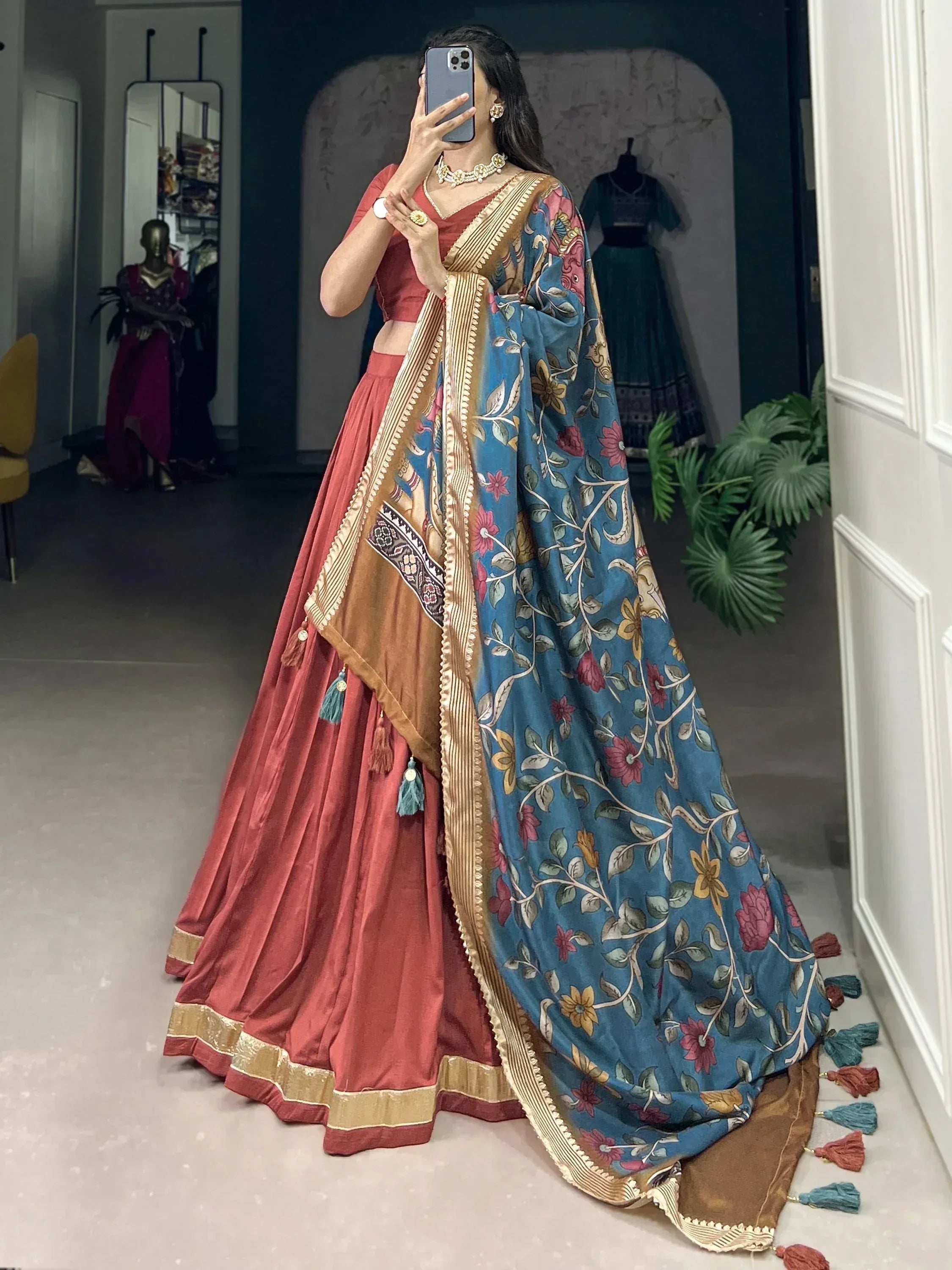 Woman in coral lehenga choli with blue floral dupatta, ethnic Indian wear for weddings or festivals
