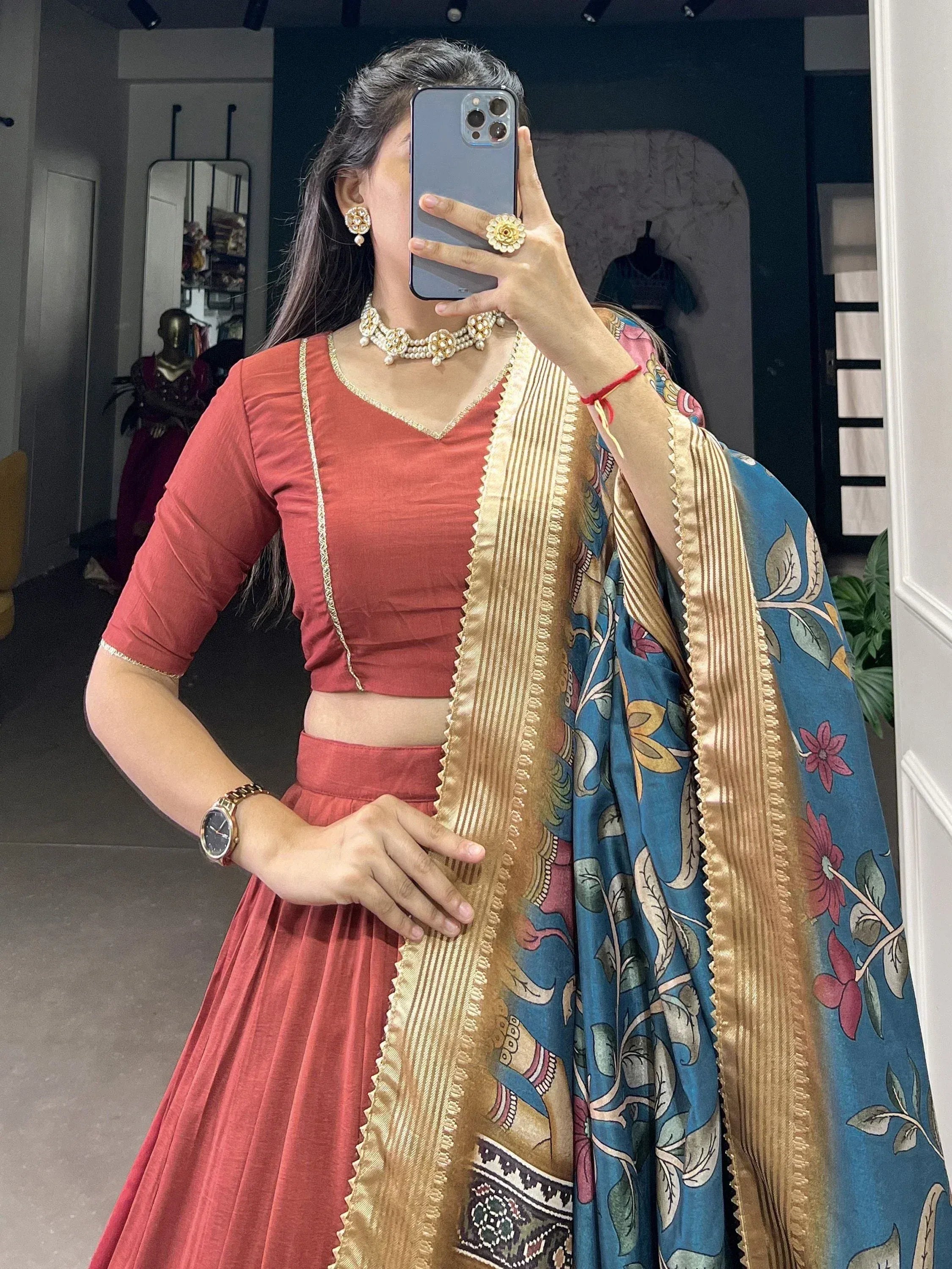 Woman in coral lehenga choli with blue floral dupatta, gold trim, and pearl jewelry for ethnic wear