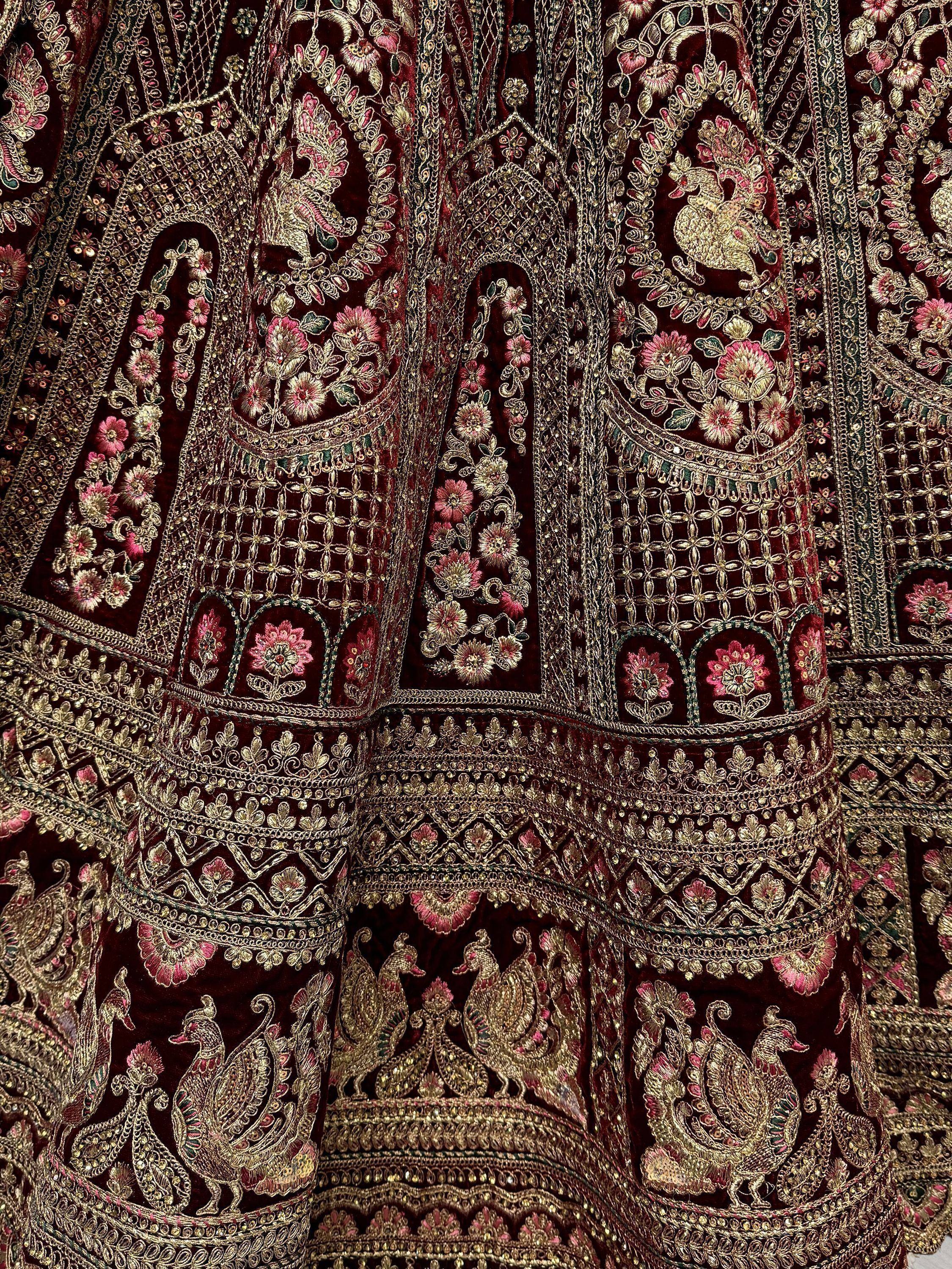 Luxury maroon velvet lehenga with heavy gold embroidery, floral motifs, and peacock designs for Indian ethnic wear.