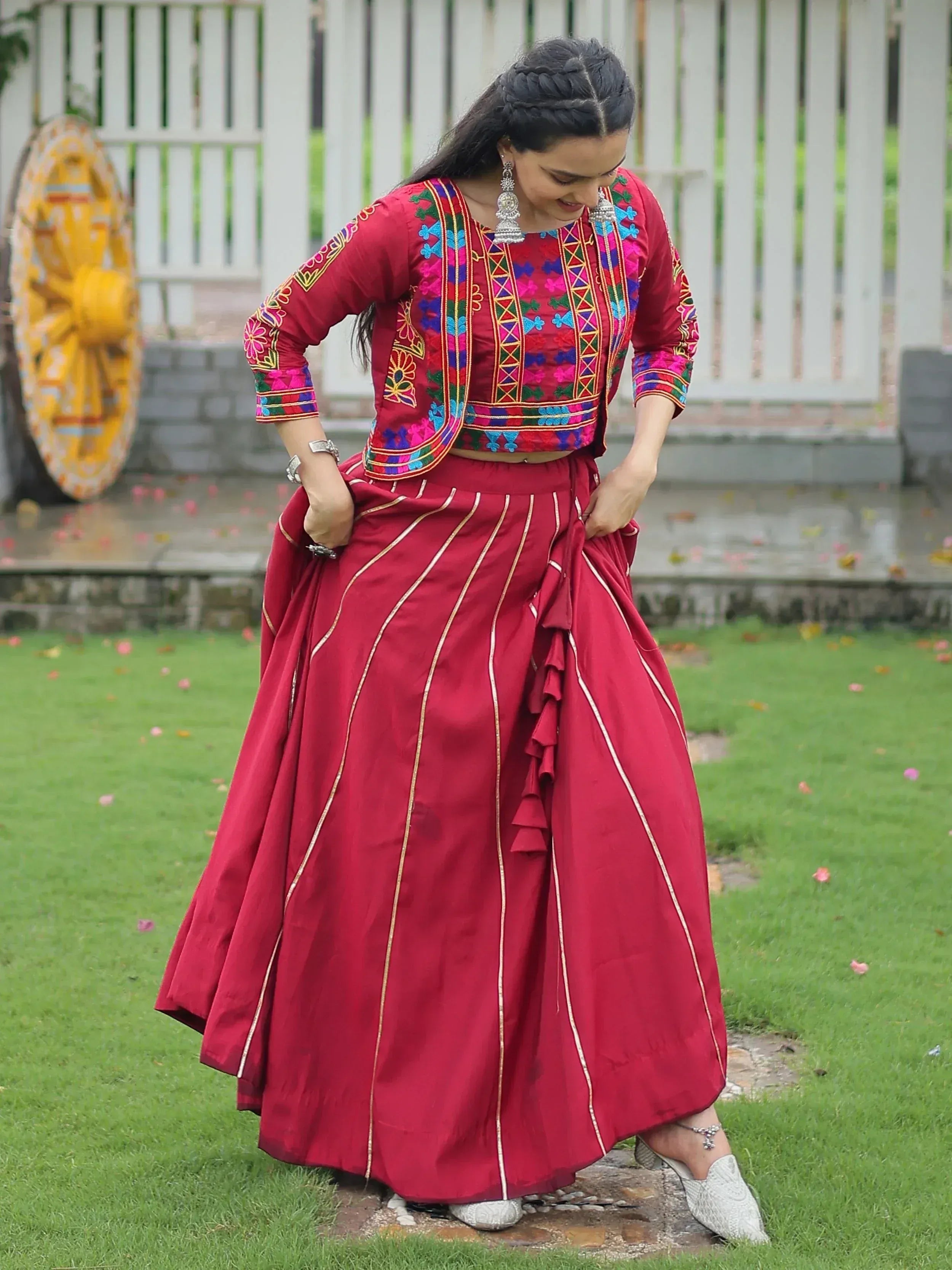 Red embroidered lehenga choli with gold stripes, styled with traditional jewelry and white mojari shoes
