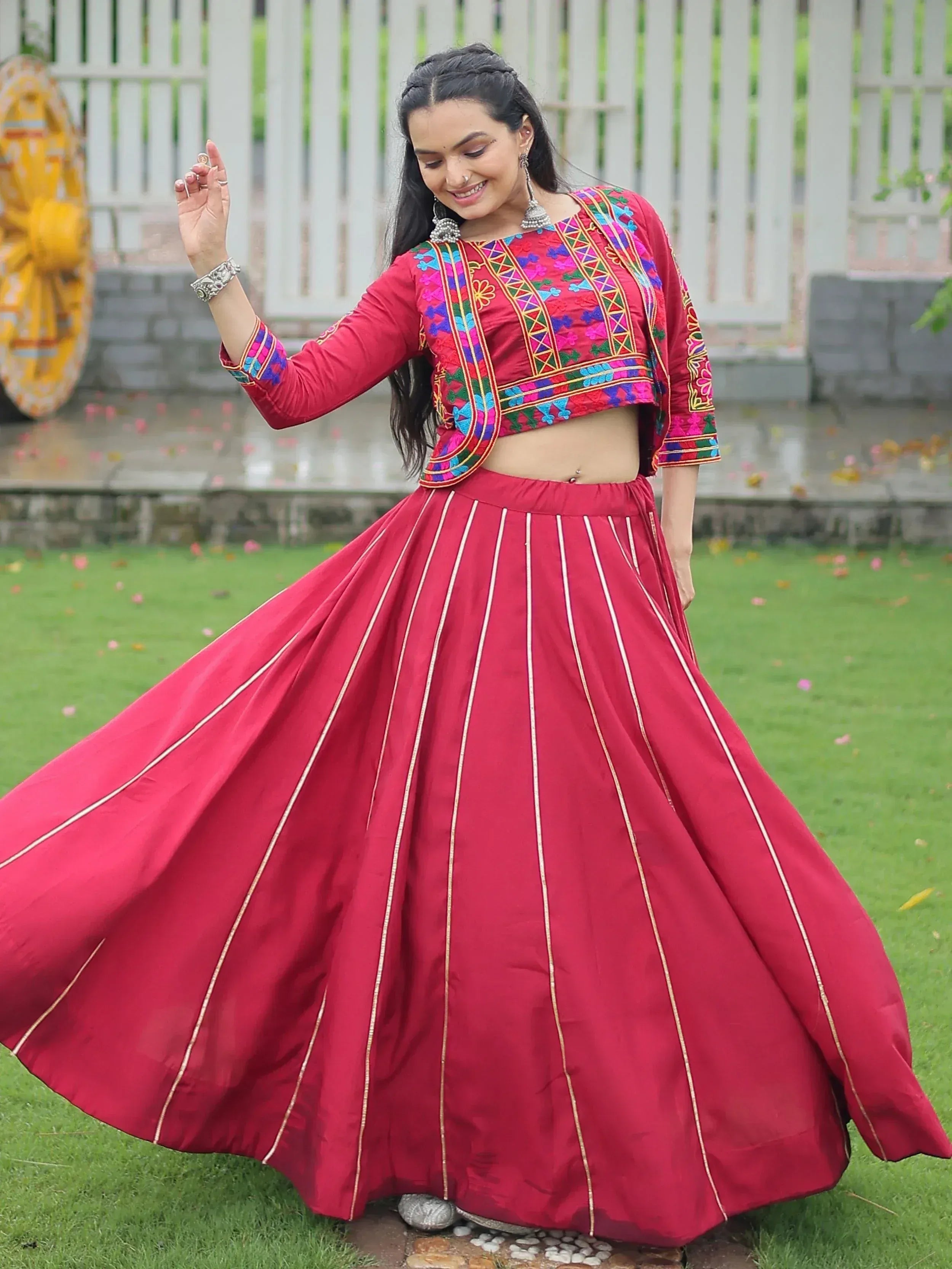 Woman in red embroidered lehenga choli with colorful floral patterns, twirling outdoors