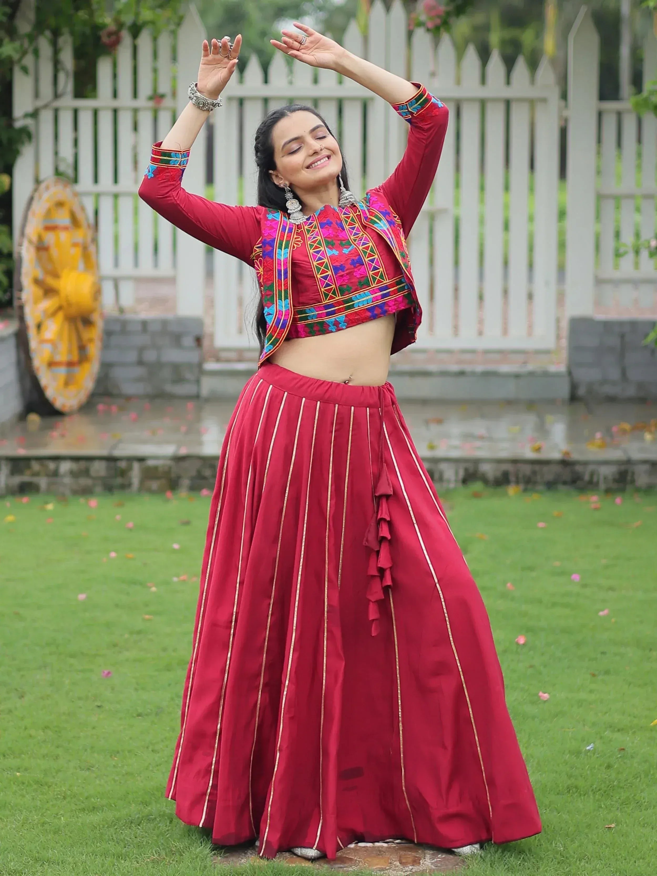 Woman in red embroidered lehenga choli with gold stripes, dancing outdoors in garden