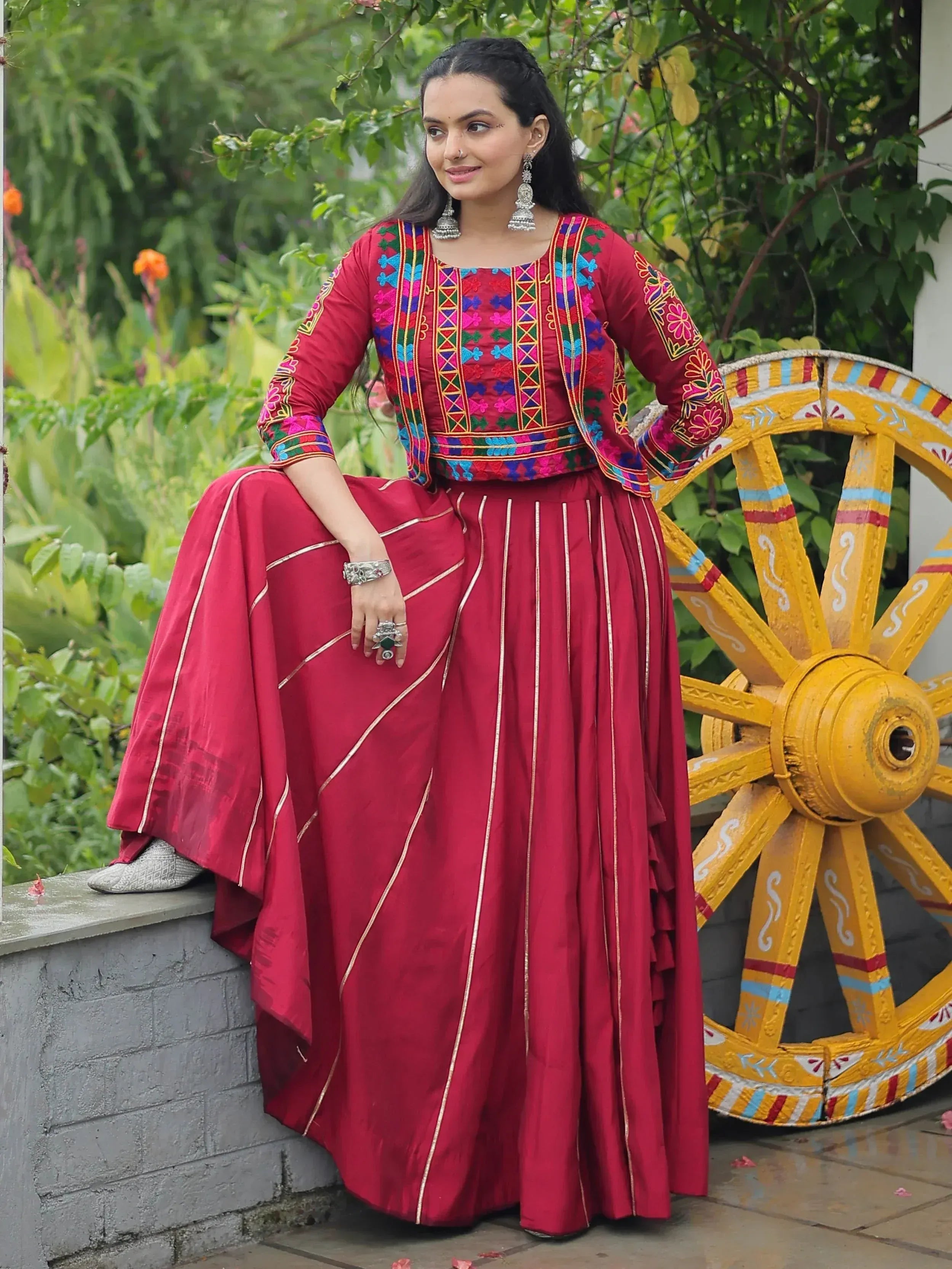 Woman in red embroidered ethnic gown with gold trim, styled with jhumka earrings and traditional jewelry