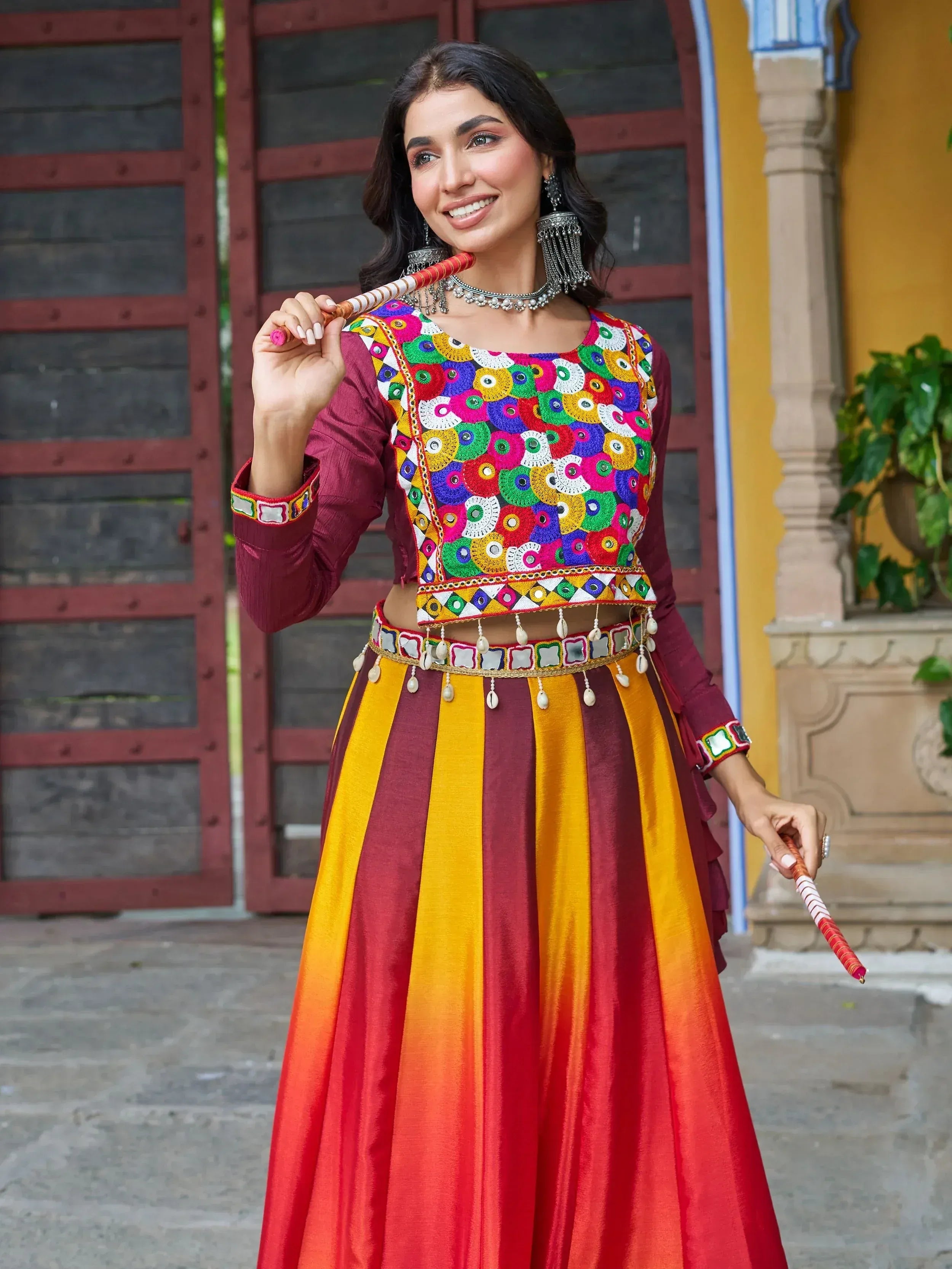 Woman in vibrant Indian ethnic wear with mirror work blouse and striped lehenga, holding dandiya sticks