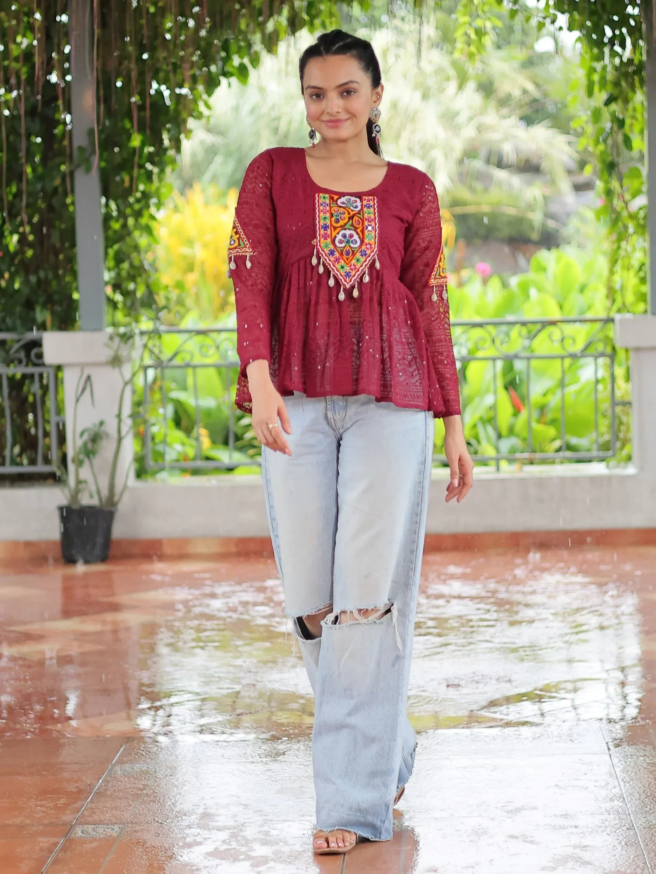 Maroon embroidered ethnic top with lace and tassels, paired with ripped jeans, styled for casual wear.