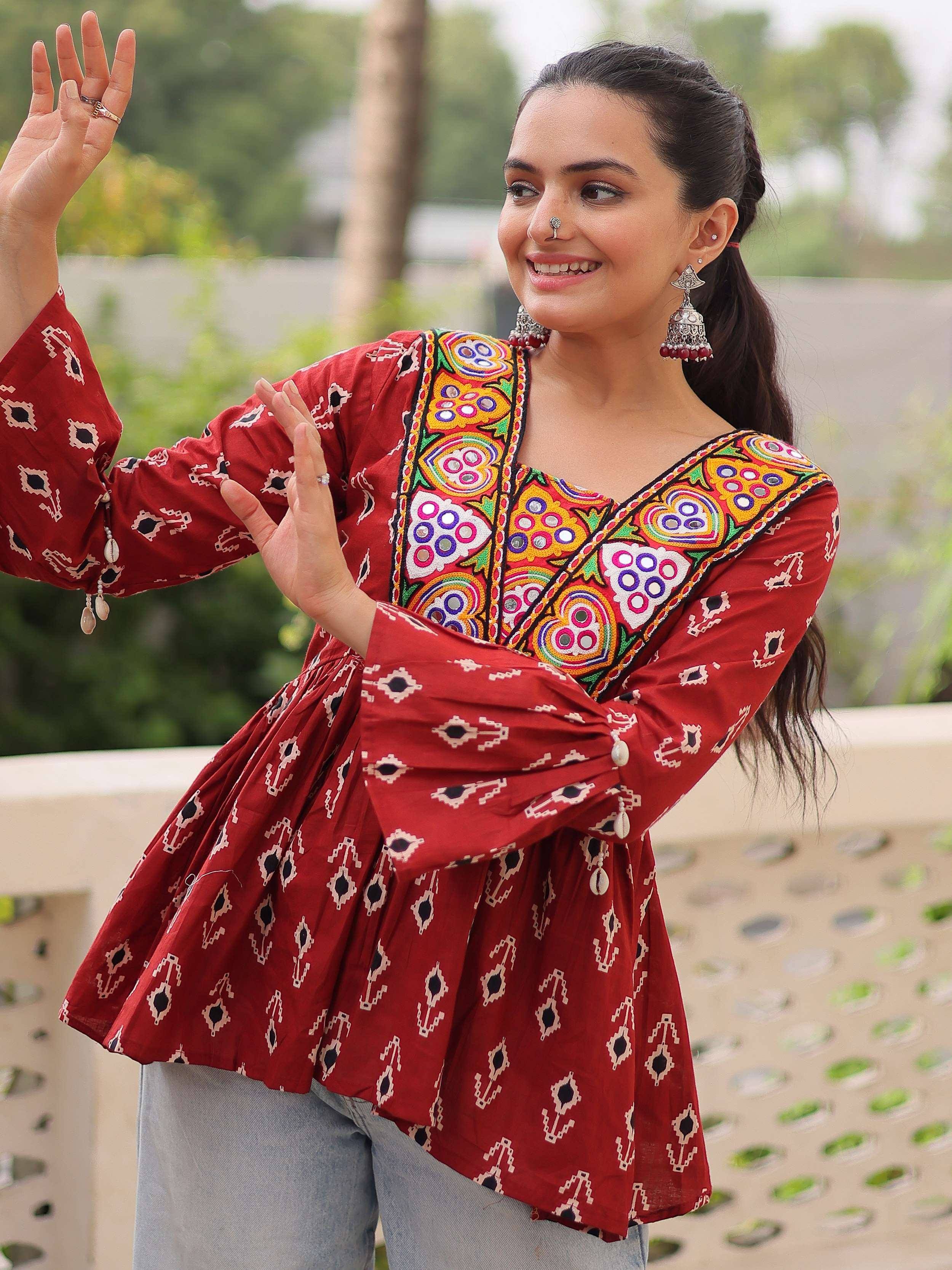 Woman in red embroidered ethnic top with mirror work, paired with jeans, showcasing Indian designer wear.