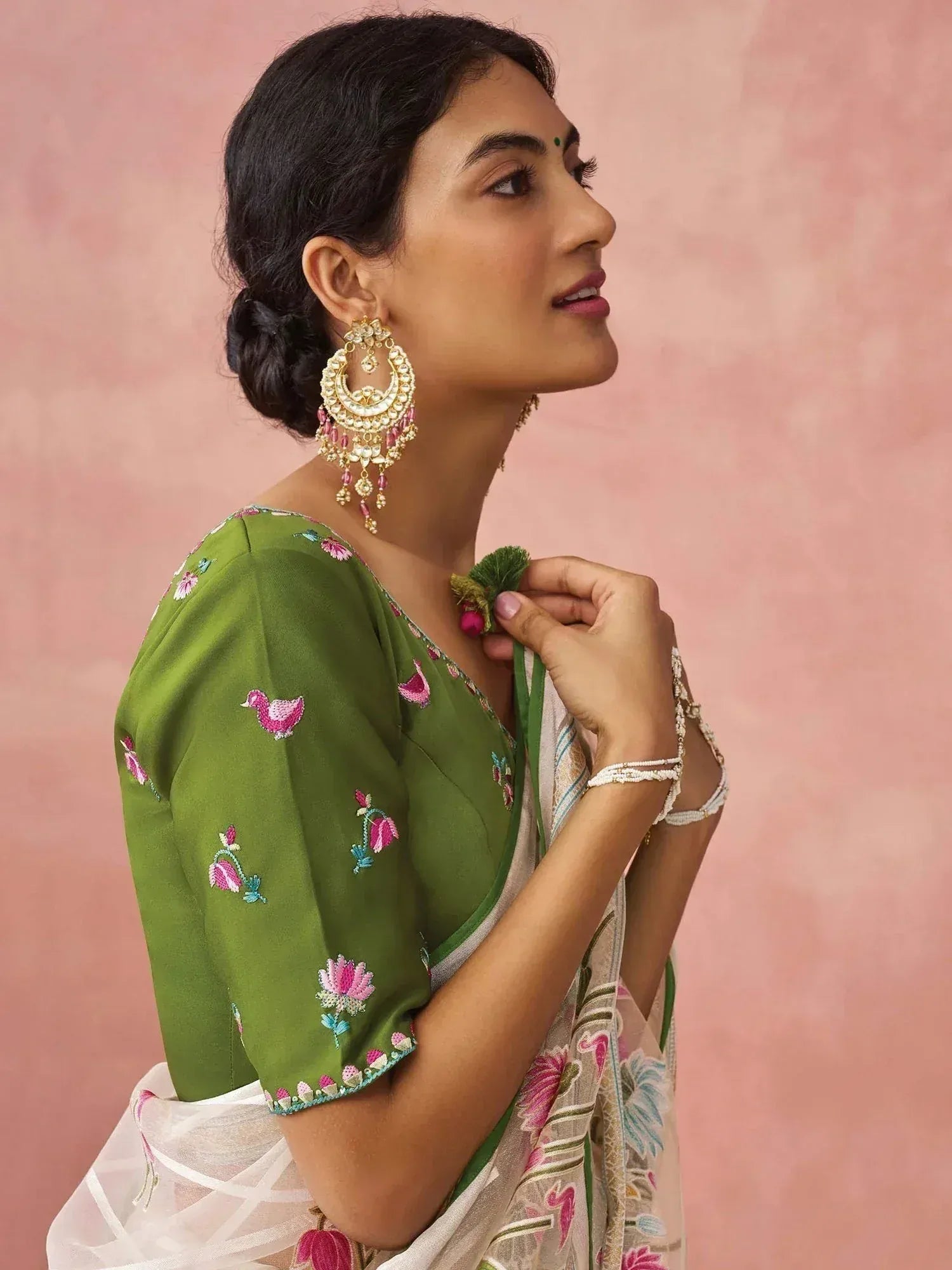 Woman in green embroidered saree blouse with floral and bird motifs, paired with statement earrings