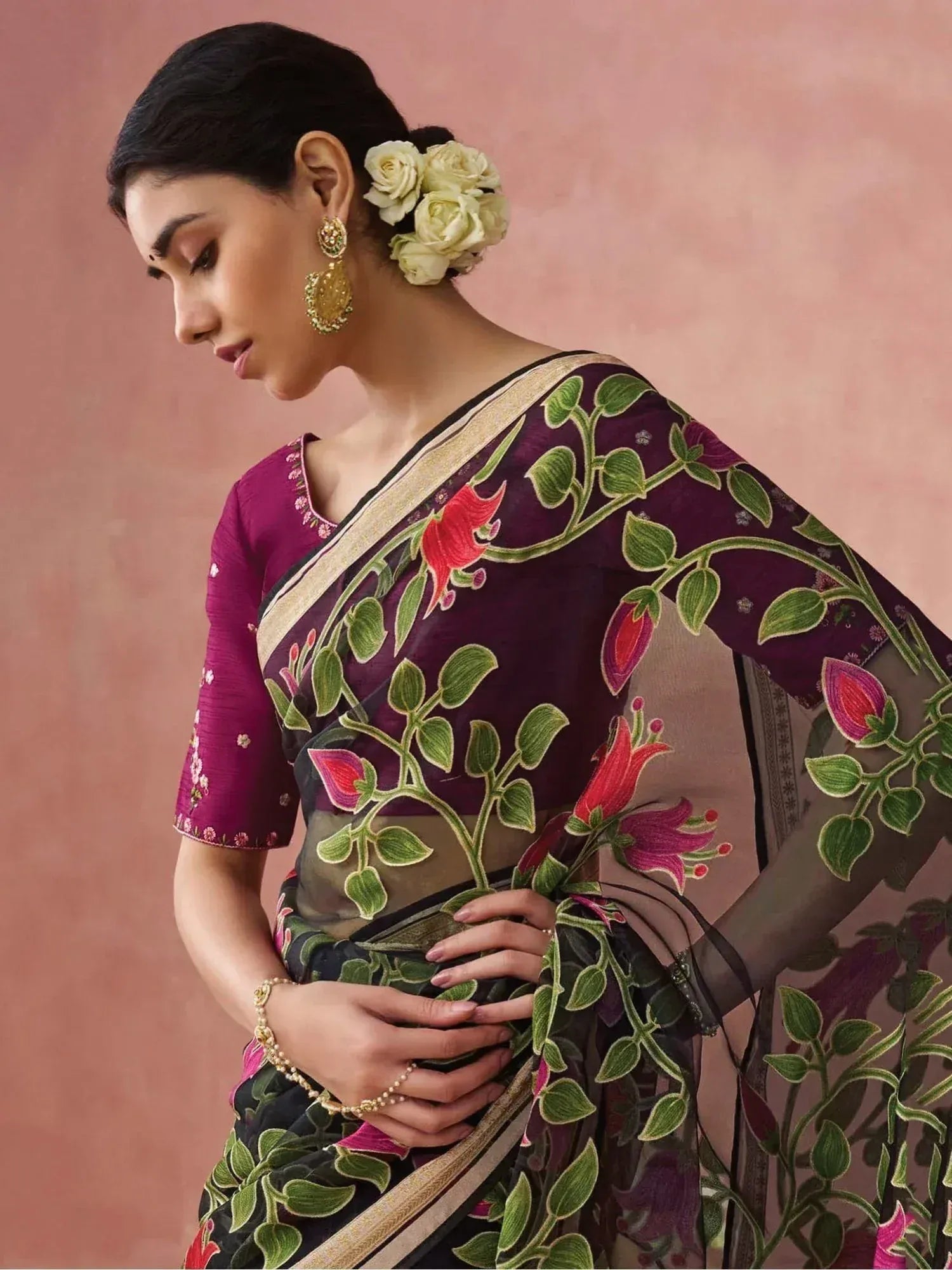 Woman in purple floral embroidered saree with gold border, styled with white roses and gold jewelry