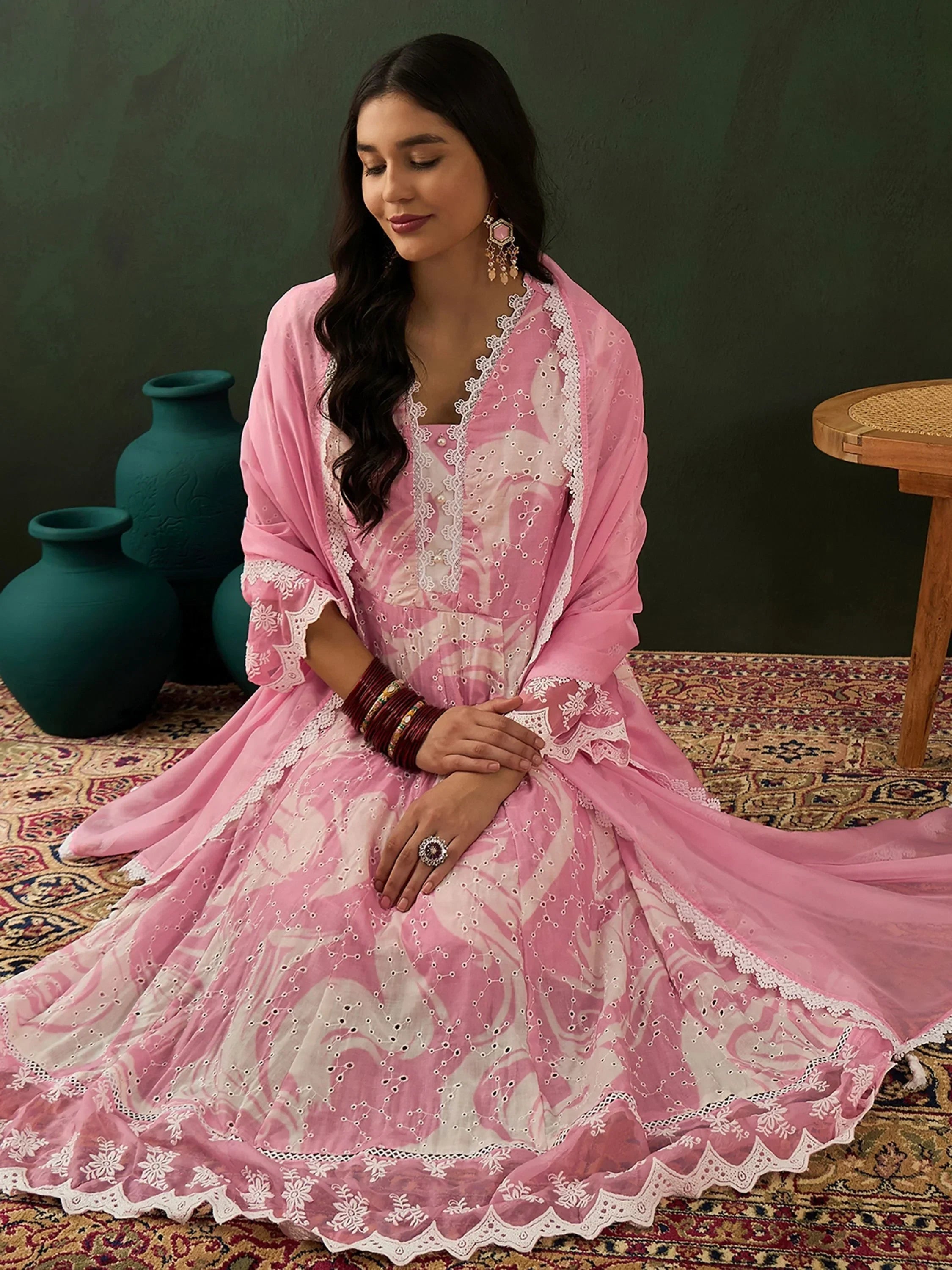 Woman in pink embroidered salwar kameez with dupatta, sitting on patterned rug