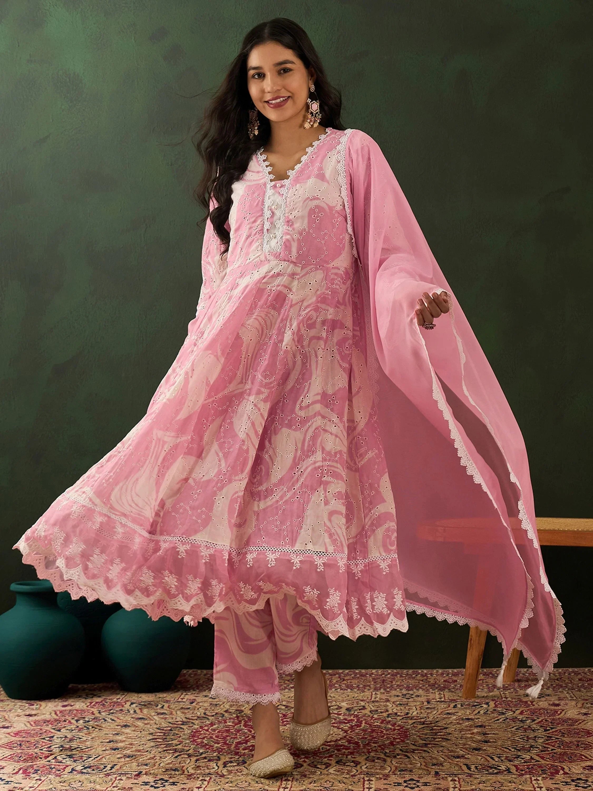 Woman wearing pink embroidered Indian ethnic suit with dupatta, standing on patterned rug