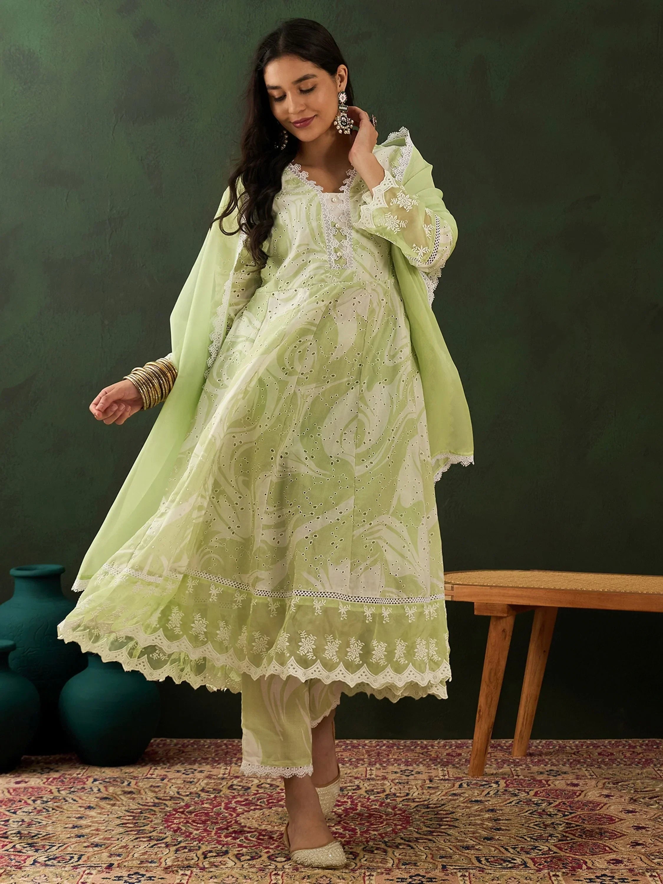 Woman in light green embroidered salwar kameez with dupatta, posing indoors on a rug