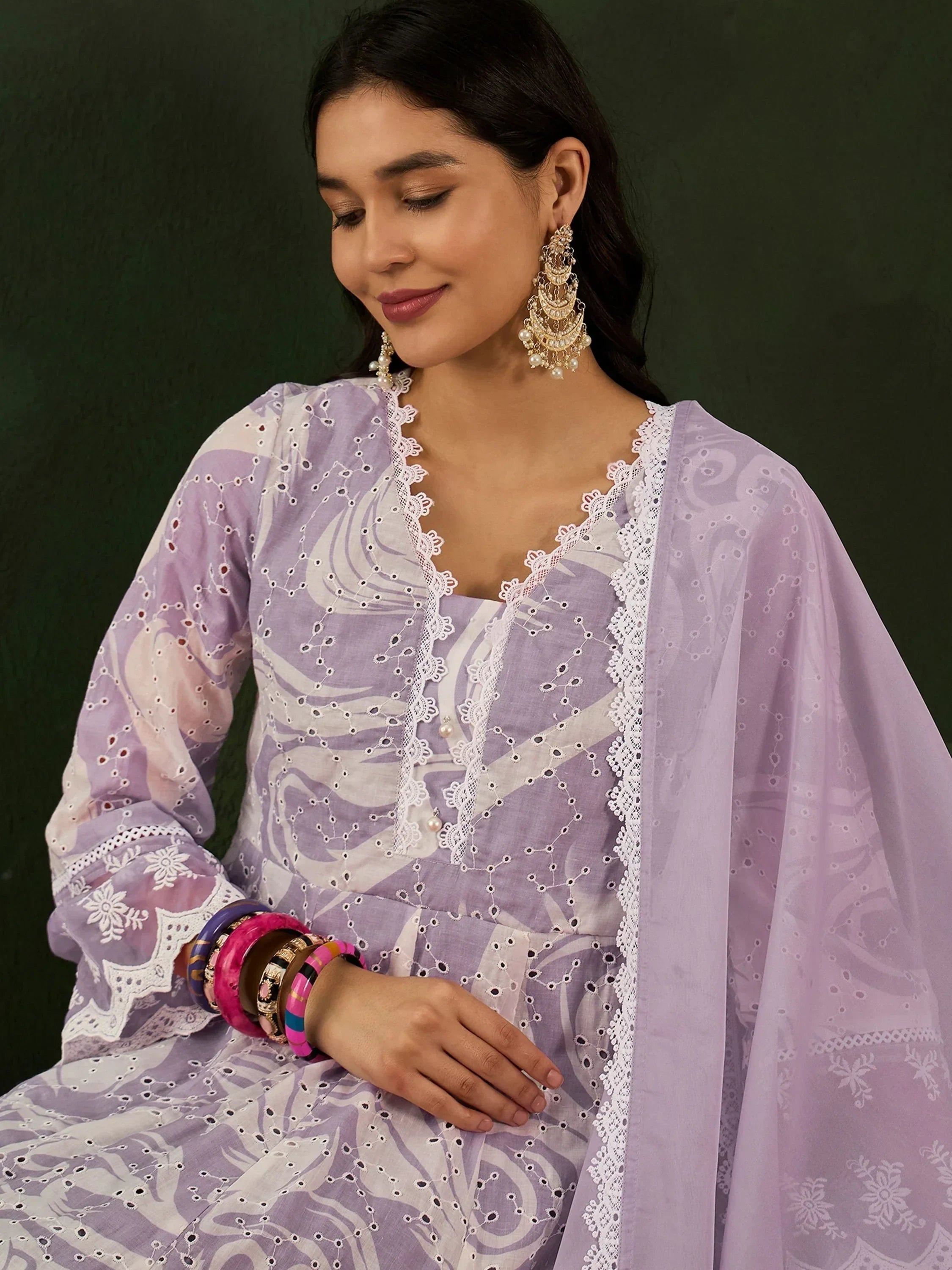 Woman in lavender embroidered salwar kameez with lace trim, statement earrings, and colorful bangles