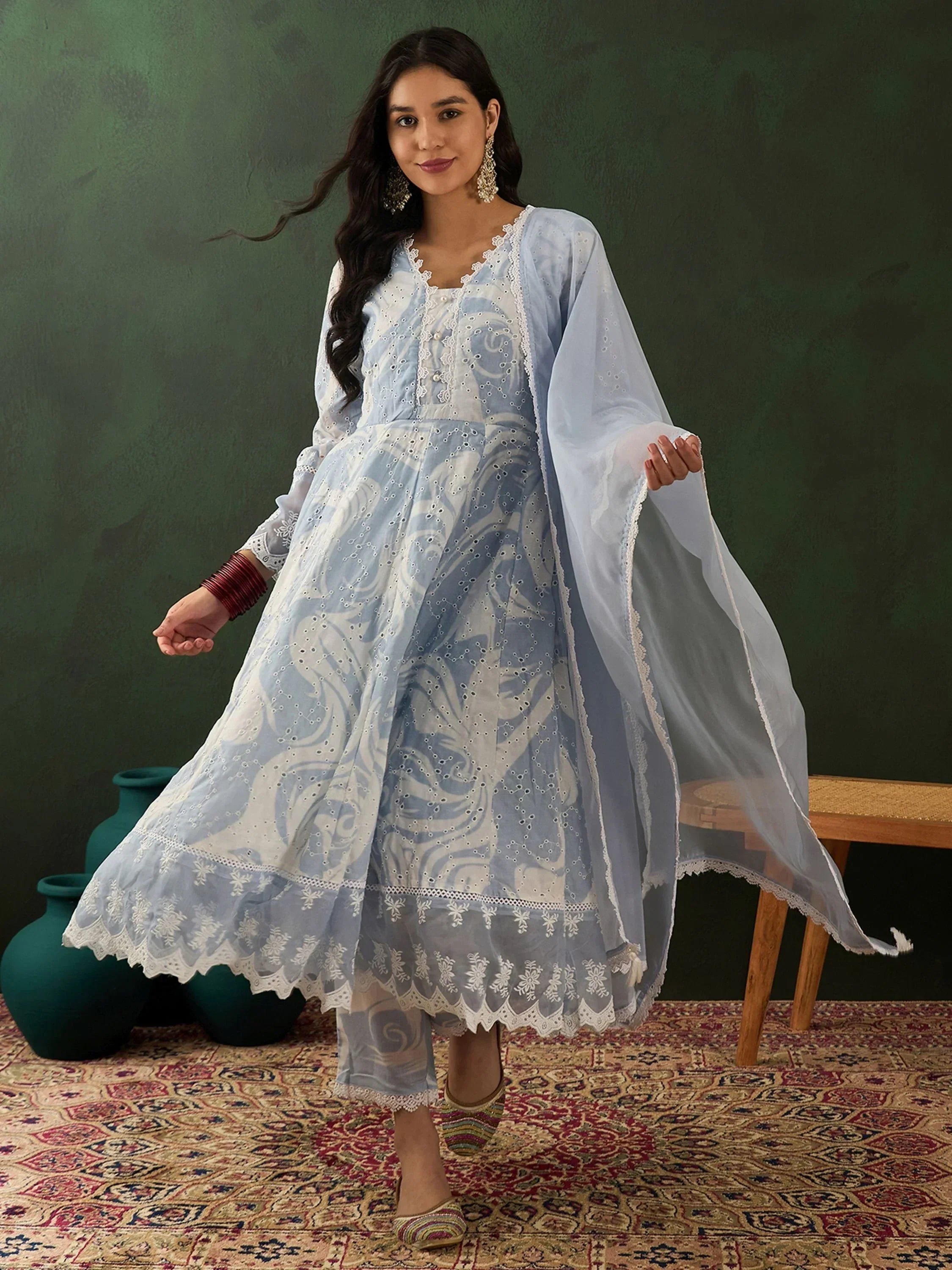 Woman wearing light blue embroidered Anarkali suit with dupatta, ethnic jewelry, and mojari shoes