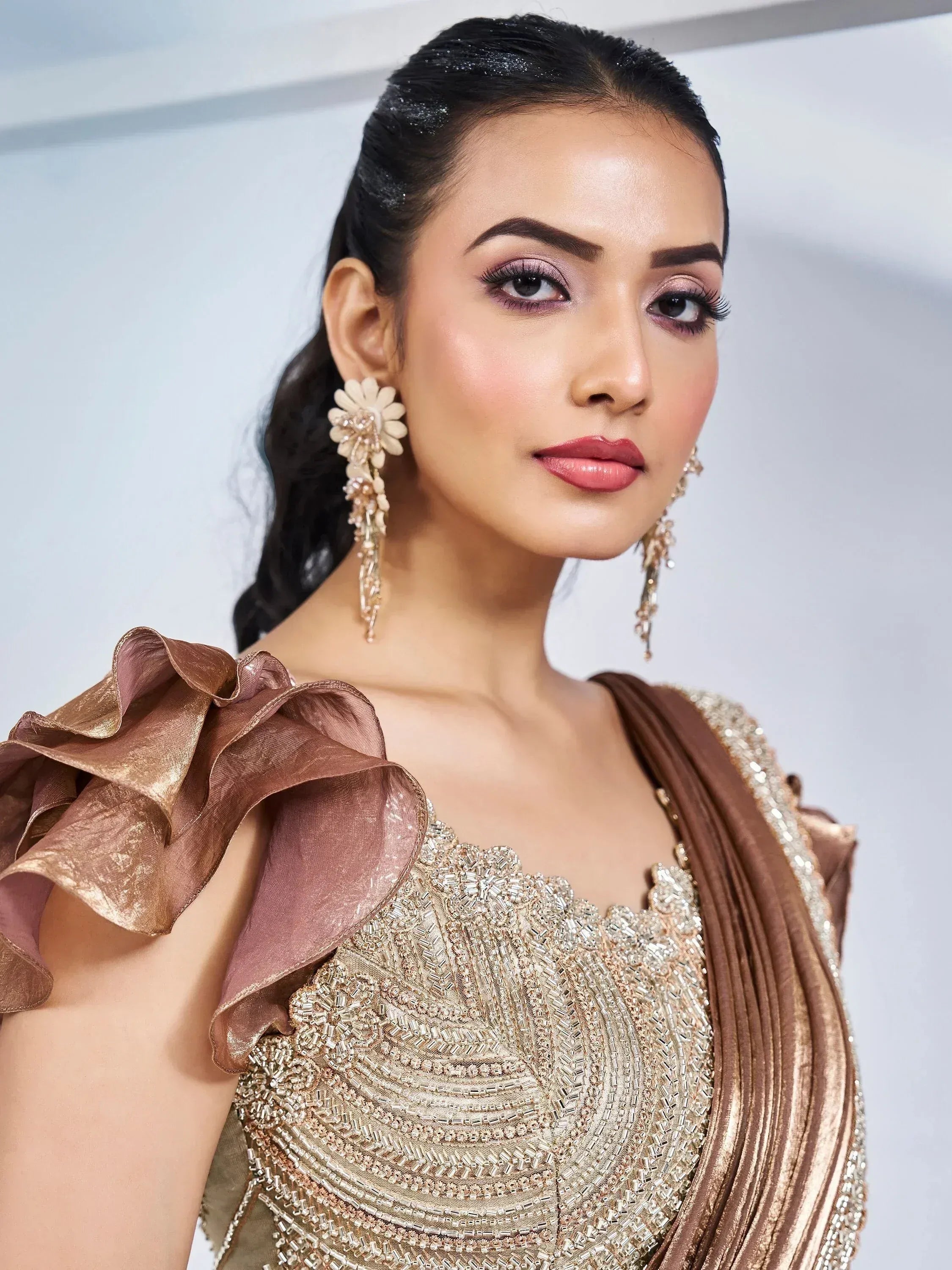 Elegant woman in gold embroidered ethnic gown with ruffled sleeves and floral earrings