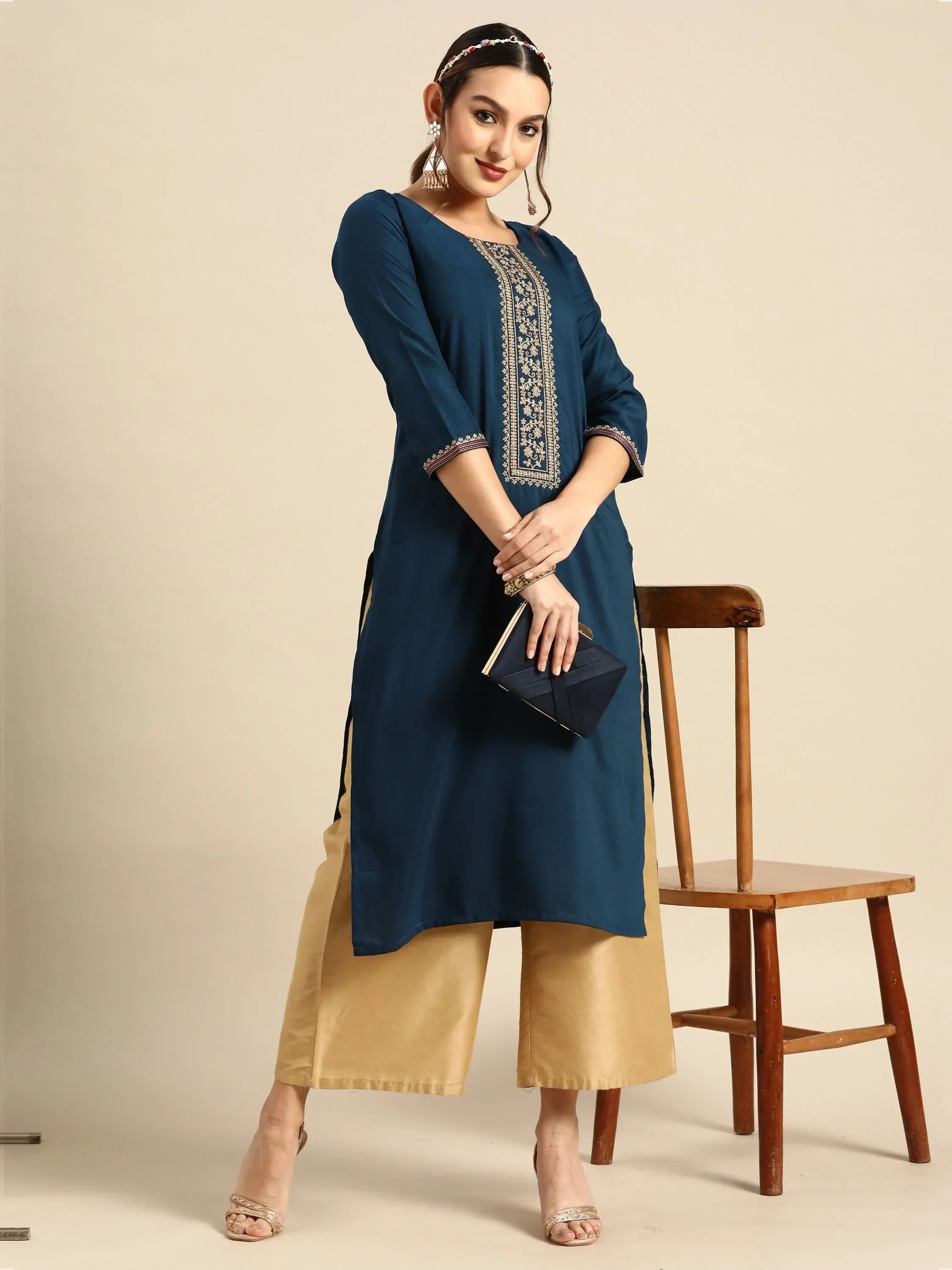 Woman in blue embroidered kurta with beige palazzo pants, holding clutch, ethnic wear