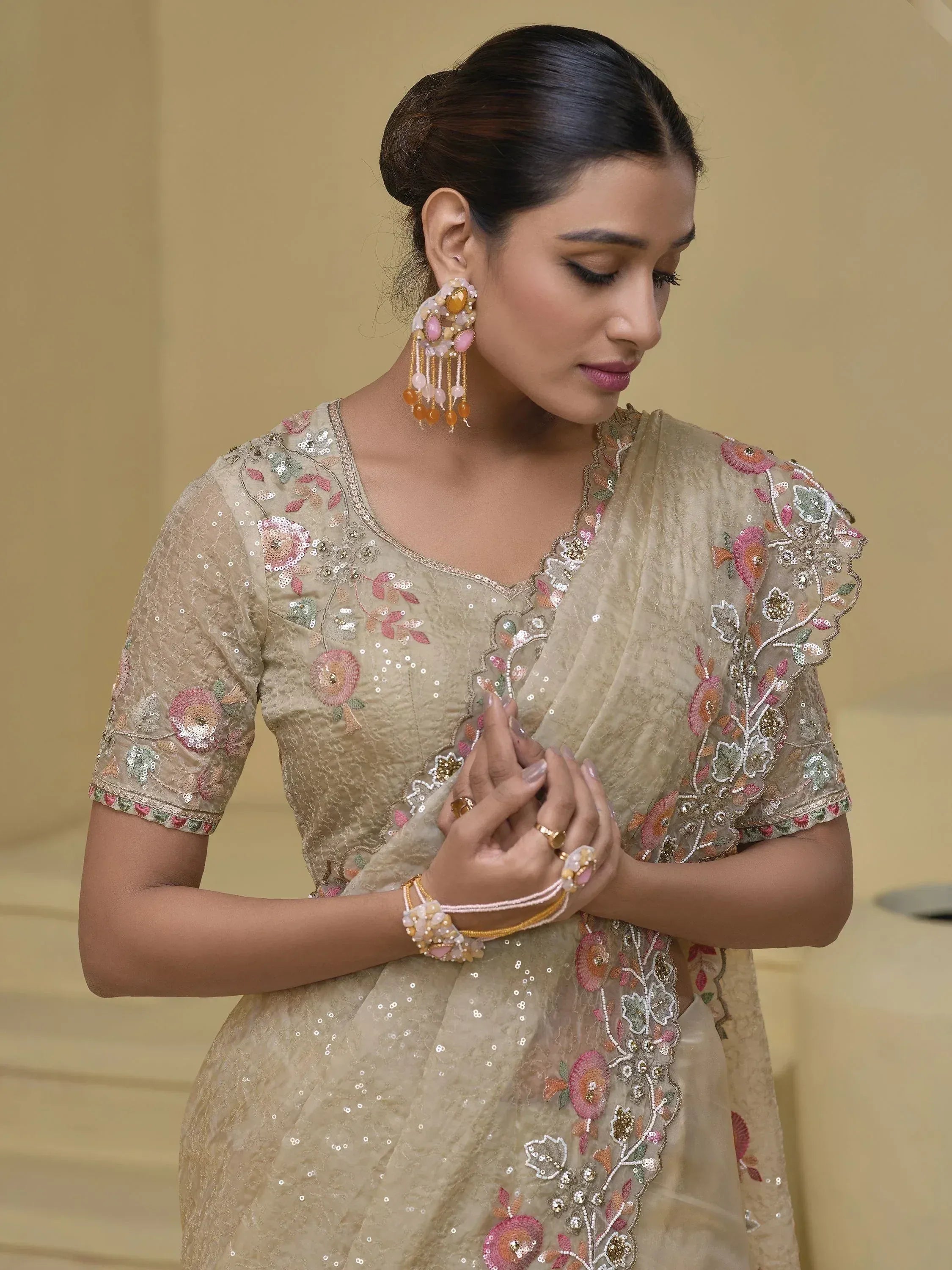 Woman in beige floral embroidered saree with sequins, statement earrings, and traditional Indian jewelry.