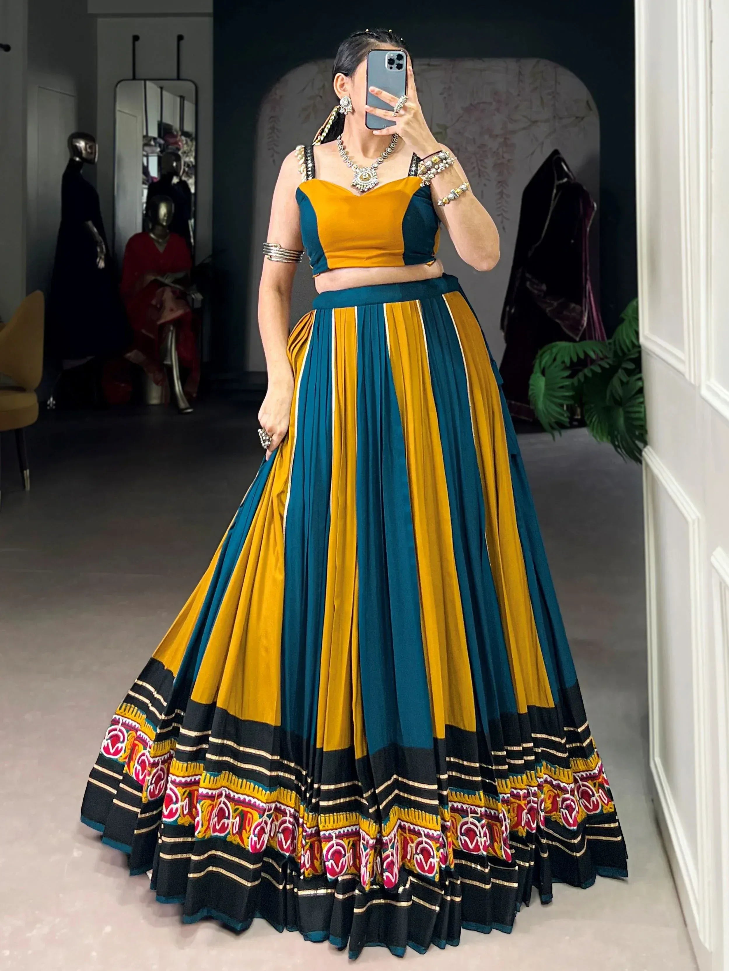 Woman in vibrant yellow and teal ethnic lehenga choli with embroidered border, perfect for festive occasions.