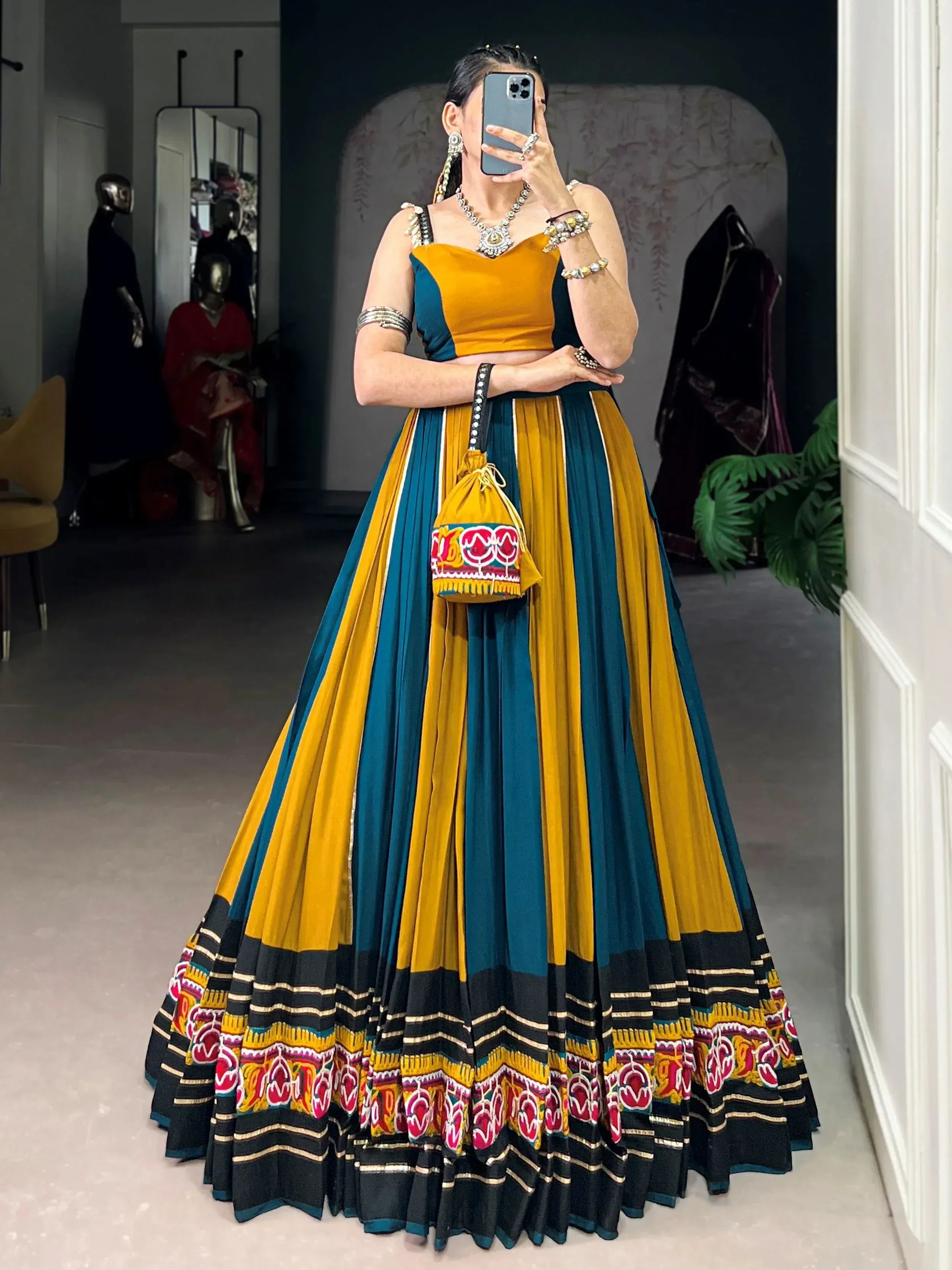 Woman in vibrant yellow and teal lehenga choli with embroidered skirt, mirror selfie in boutique