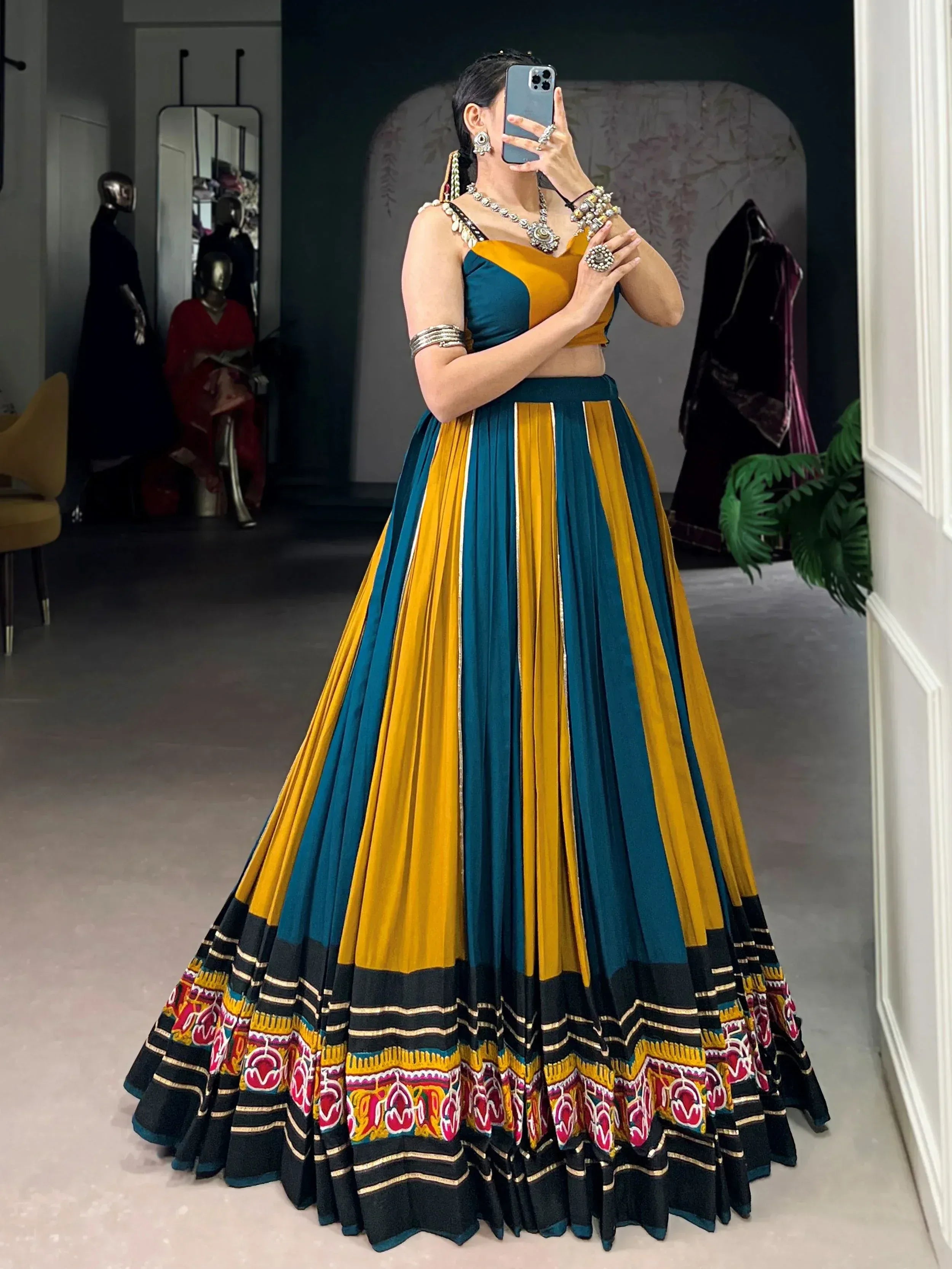 Woman in vibrant teal and mustard yellow lehenga choli with embroidered border, perfect for Indian ethnic wear.