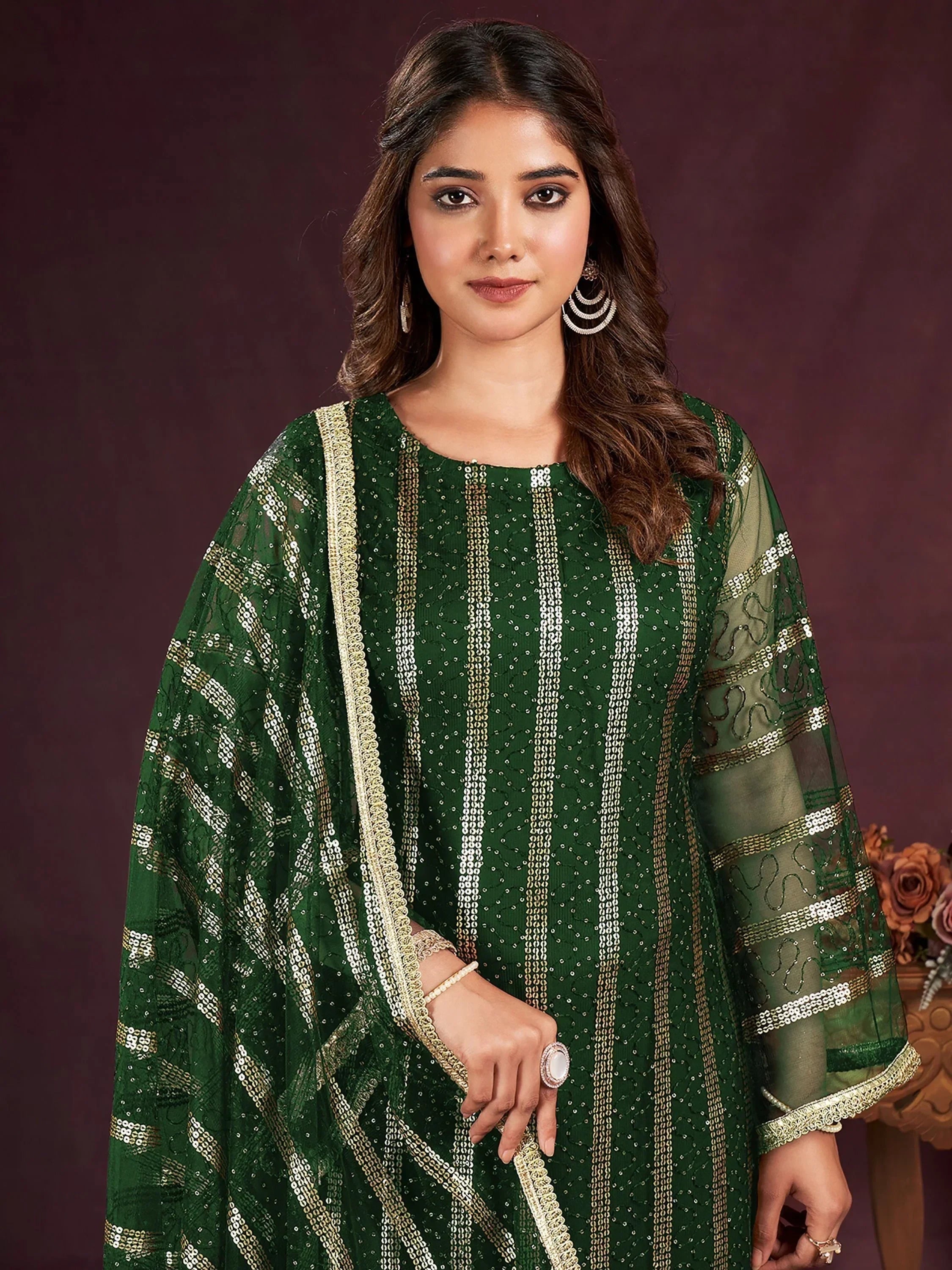 Woman in green sequin embroidered salwar kameez with matching dupatta, posing indoors