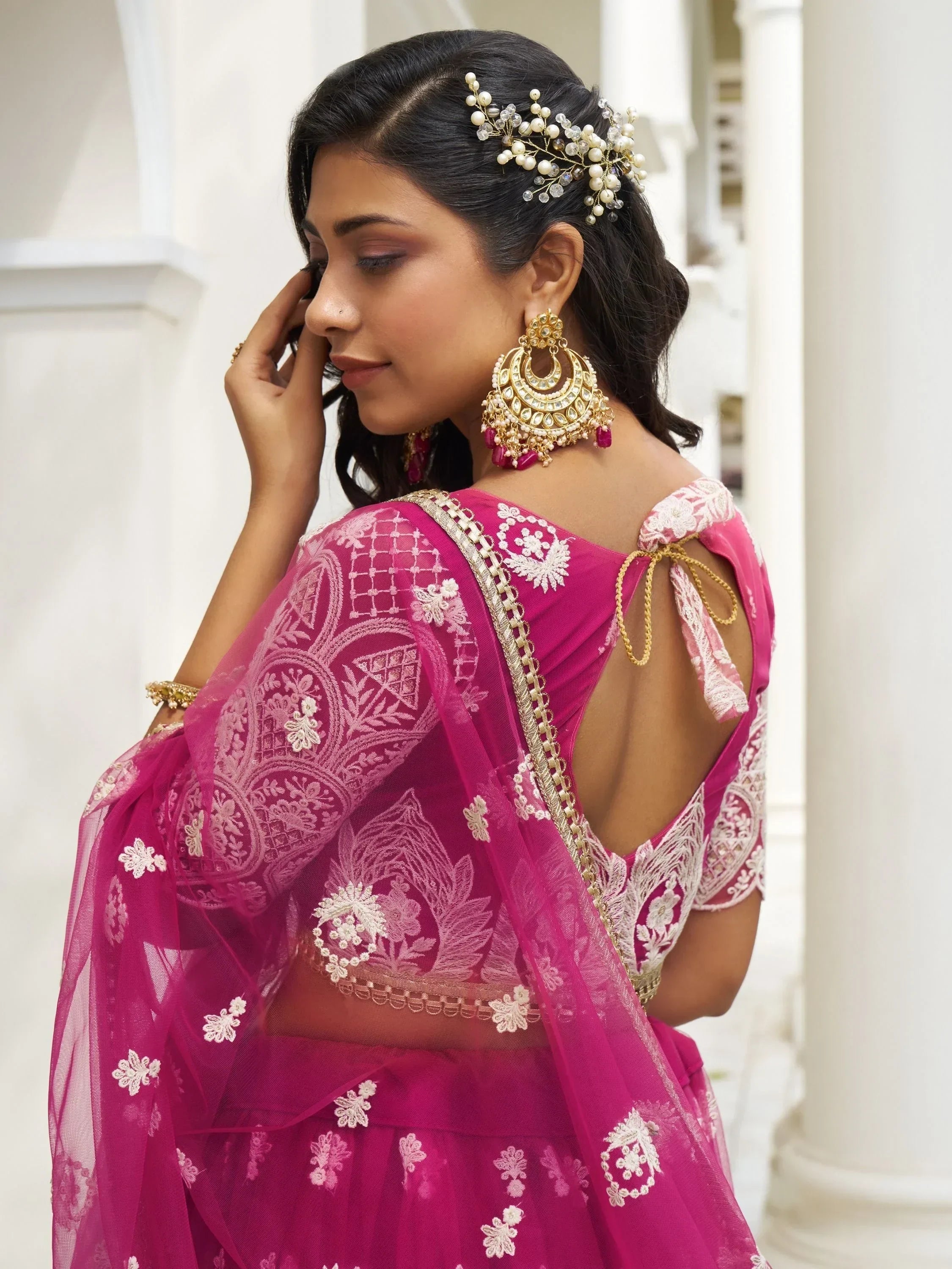 Pink embroidered lehenga choli with gold jewelry and floral hair accessory for Indian ethnic wear