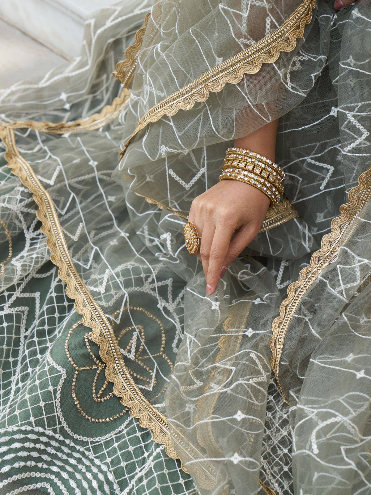 Elegant olive green lehenga with white and gold embroidery, paired with traditional bangles and ring.