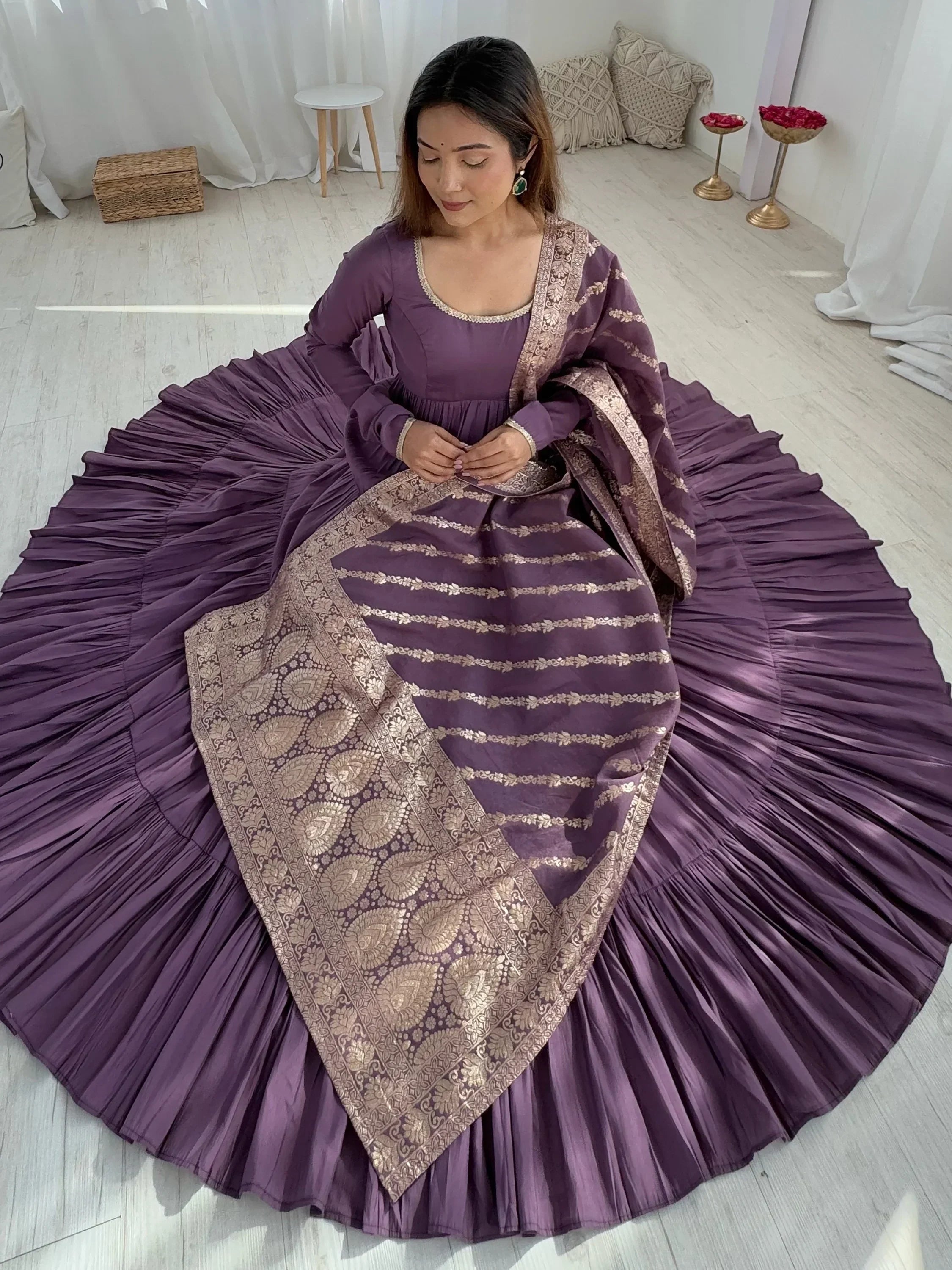 Woman wearing a purple ethnic gown with gold embroidery, sitting on a pleated flared dress