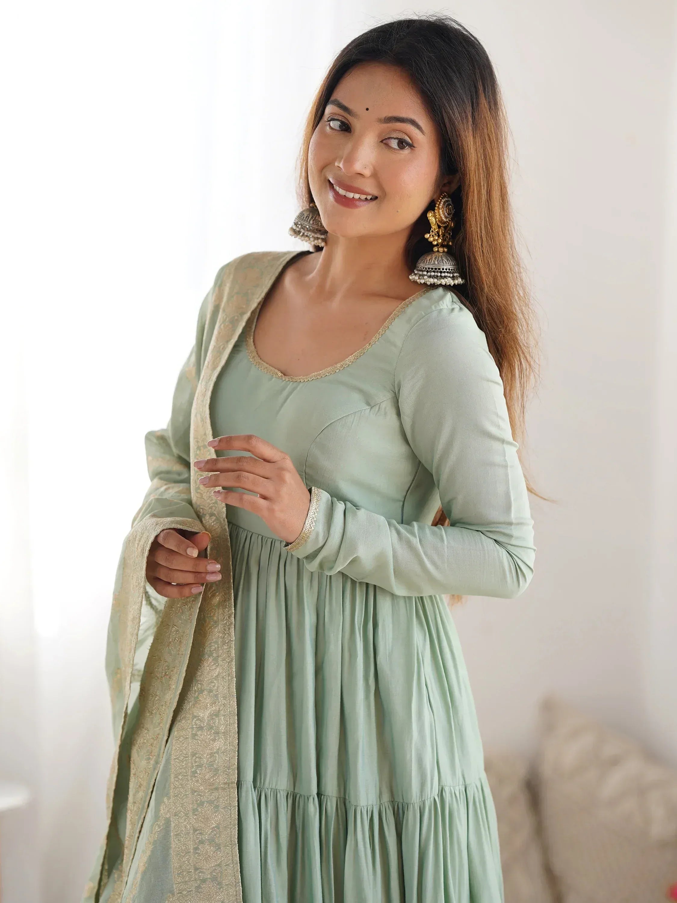 Woman in pastel green Anarkali dress with golden dupatta and traditional jhumka earrings
