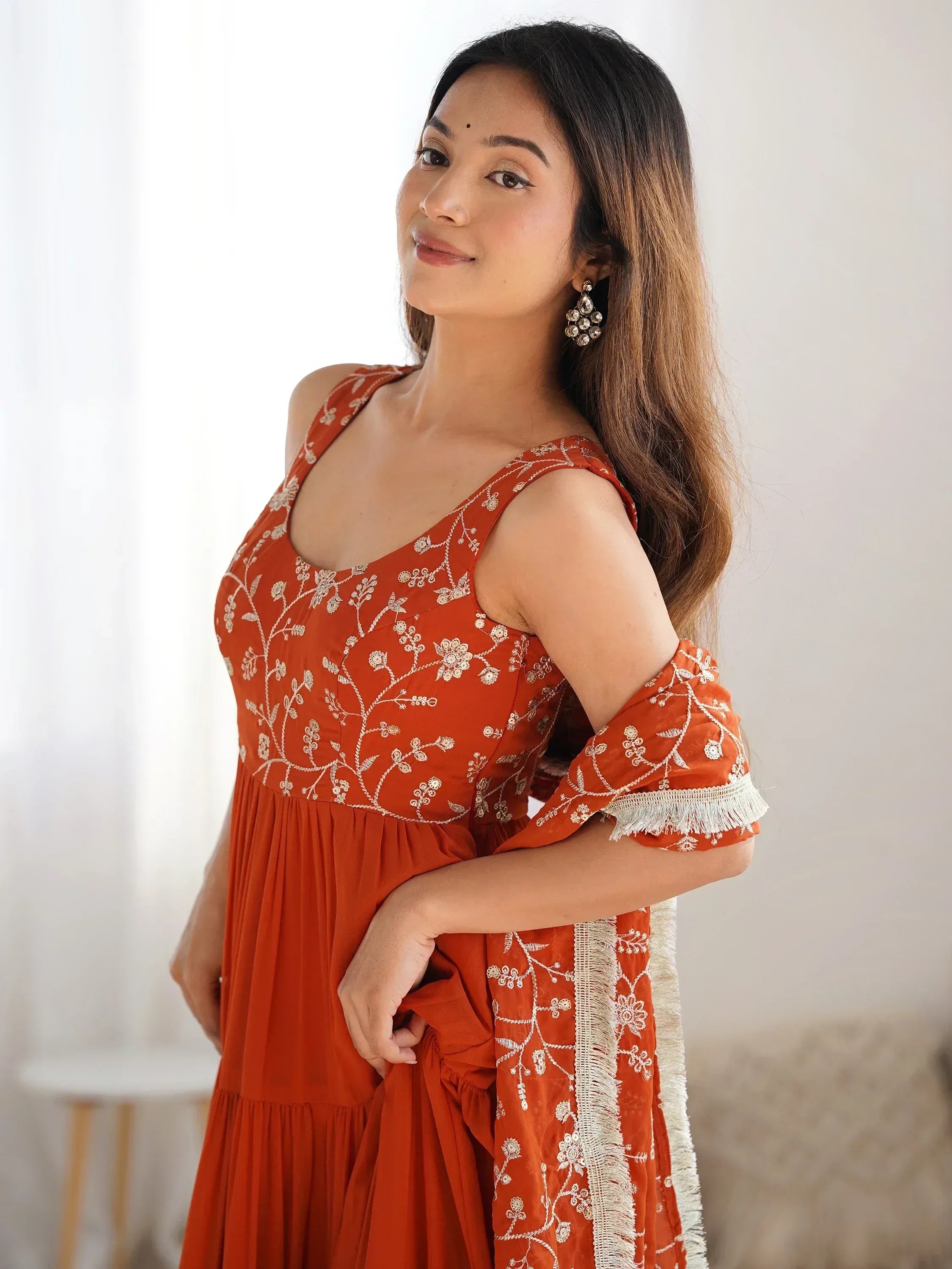 Woman in rust orange ethnic gown with white floral embroidery and cold shoulder sleeves