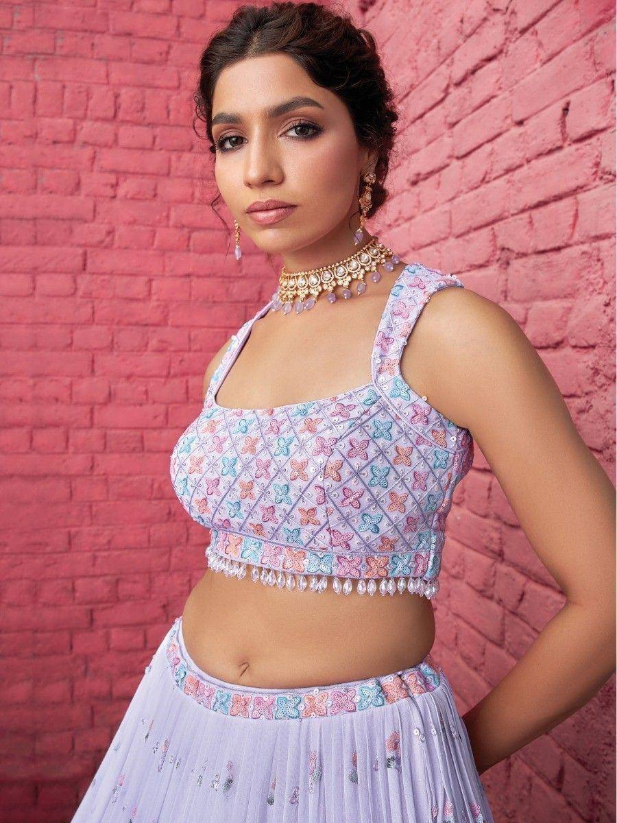 Pastel butterfly-embroidered lehenga choli with pearl trim, styled with gold jewelry against pink brick wall