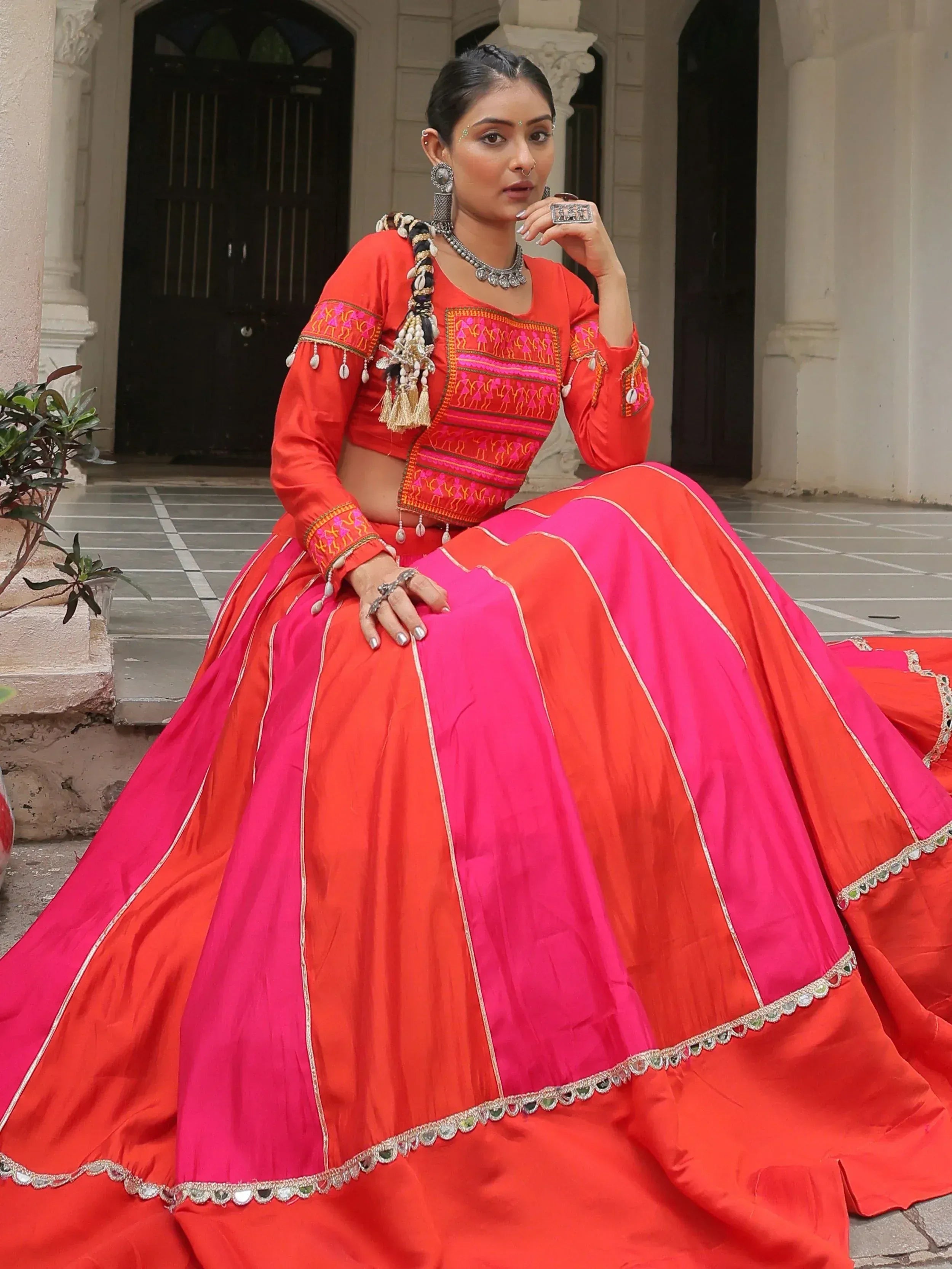 Vibrant red and pink designer lehenga choli with intricate embroidery and mirror work, perfect for festive occasions.