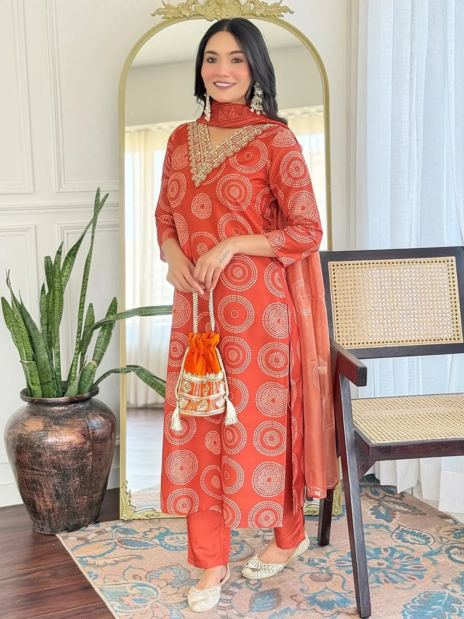 Woman in orange printed salwar kameez with gold embroidery, matching dupatta and potli bag, ethnic Indian wear