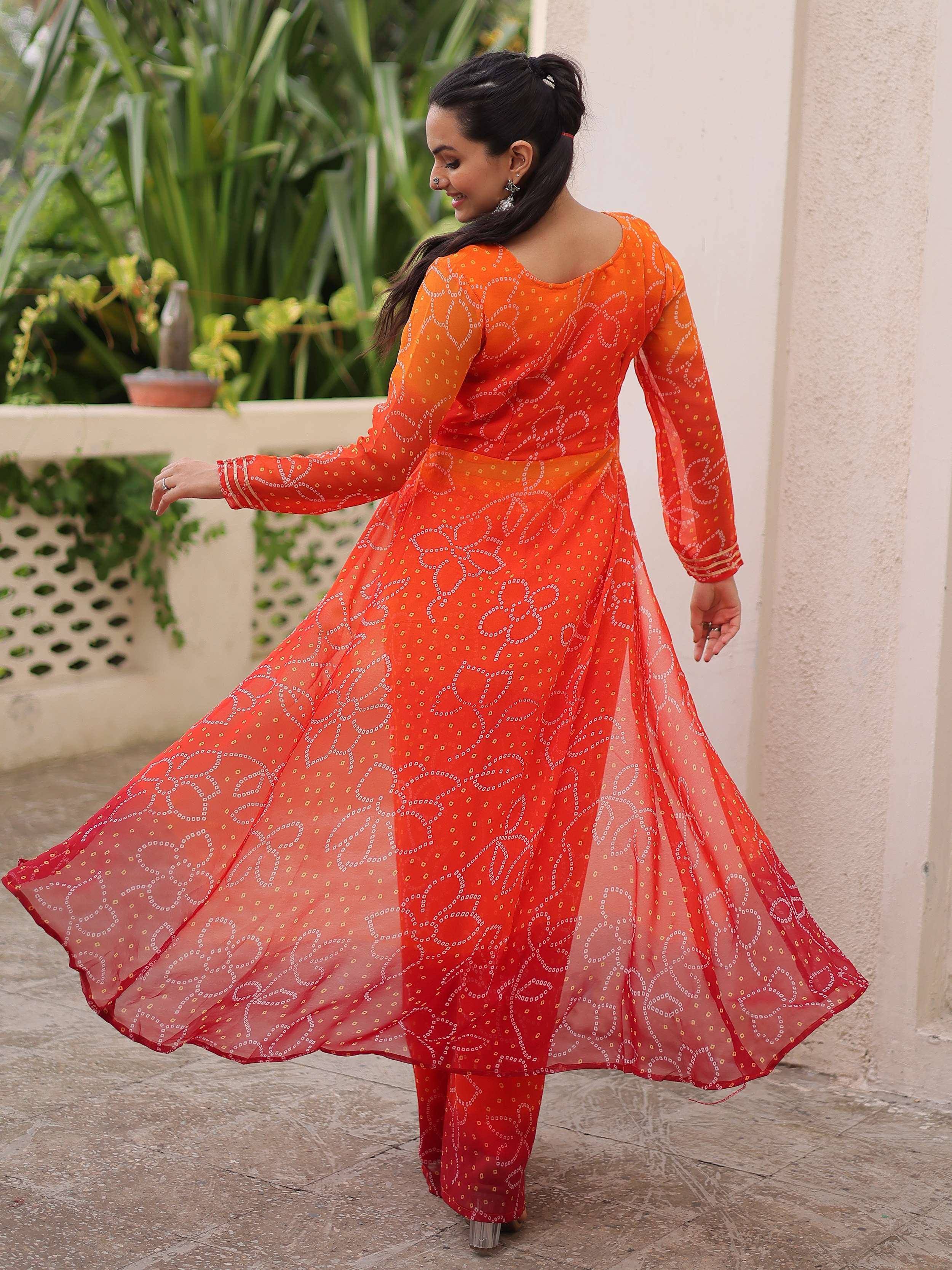 Woman twirling in vibrant orange printed anarkali suit with flared skirt, perfect for ethnic occasions